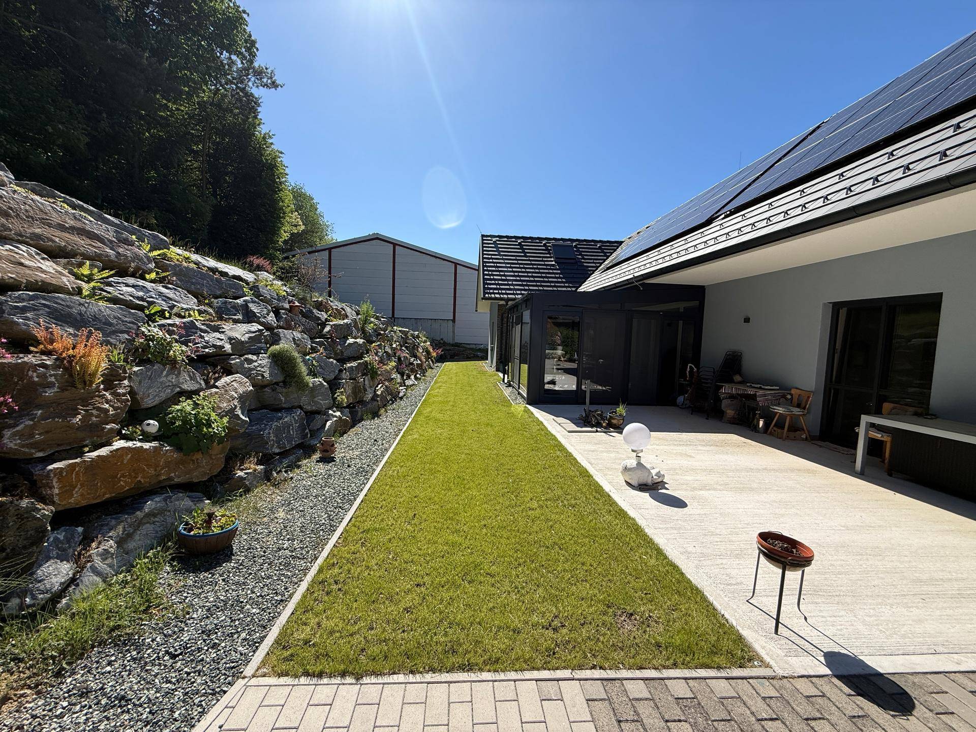 Moderne Hausfassade mit Solaranlage, gepflasterter Terrasse und gepflegtem Rasenbereich.