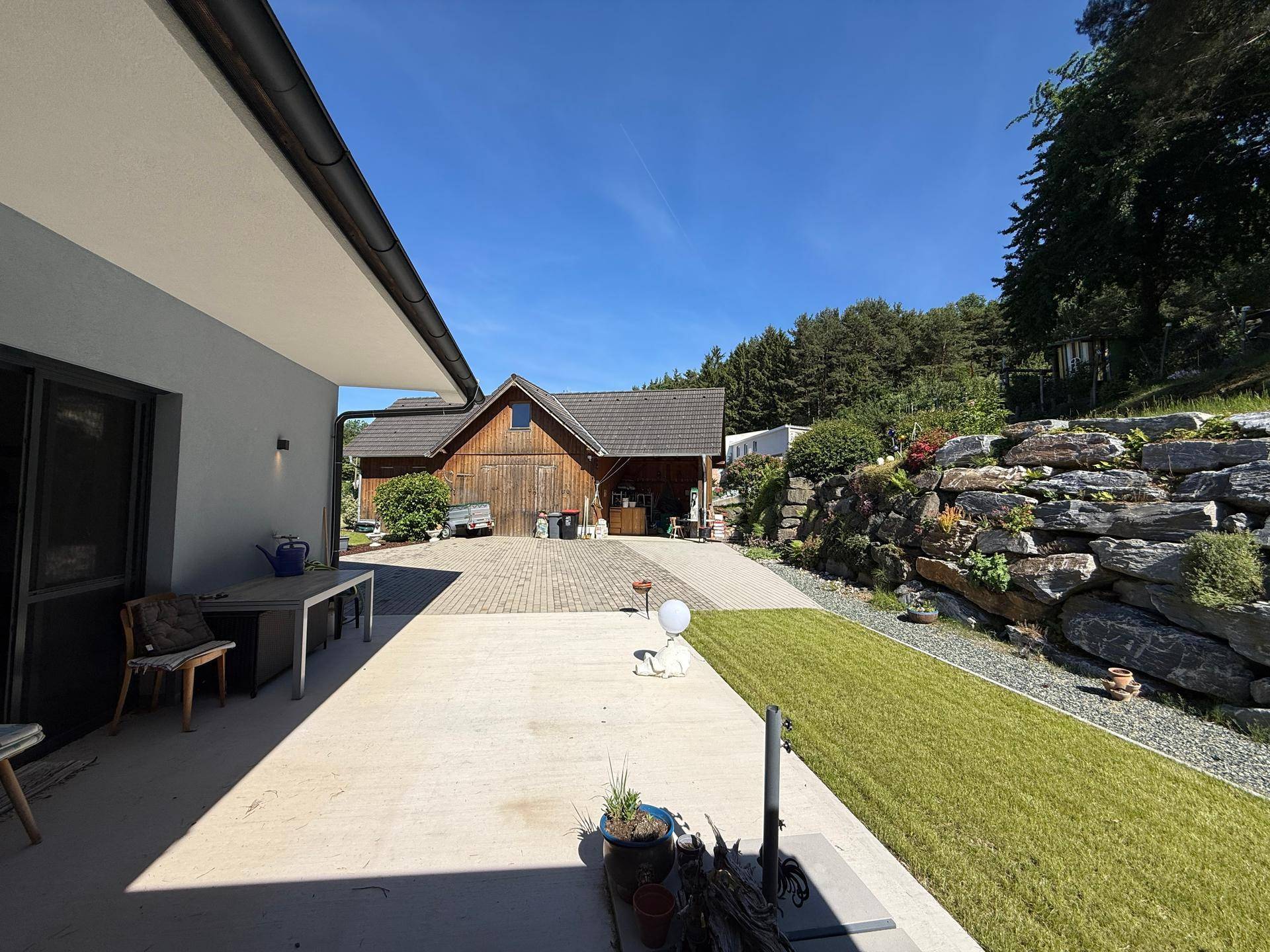 Große gepflasterte Terrasse am Haus mit Blick auf ein rustikales Holzgebäude und die Landschaft.
