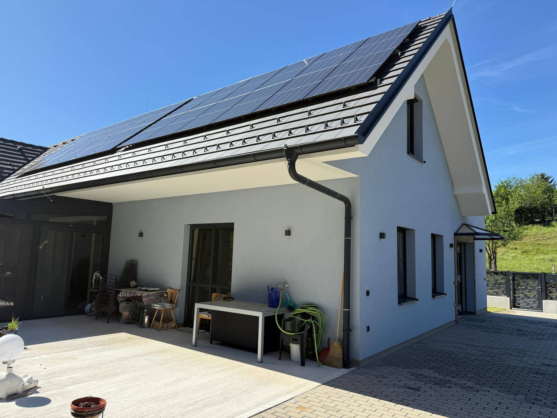 Moderne Hausfassade mit Solaranlage auf dem Dach und großzügiger gepflasterter Terrasse.