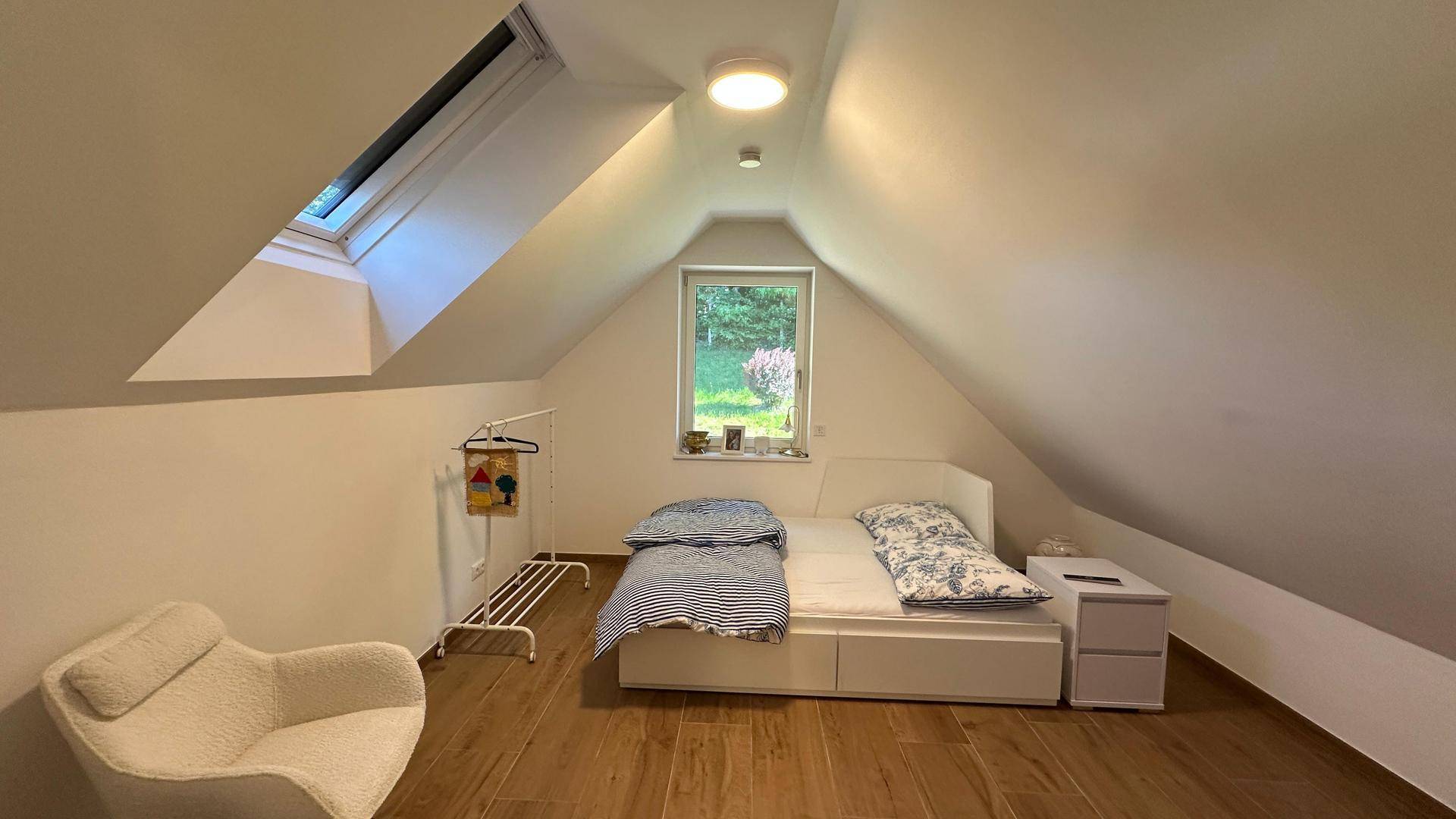 Helles Schlafzimmer im Dachgeschoss mit Dachschräge, Holzboden und Blick ins Grüne.