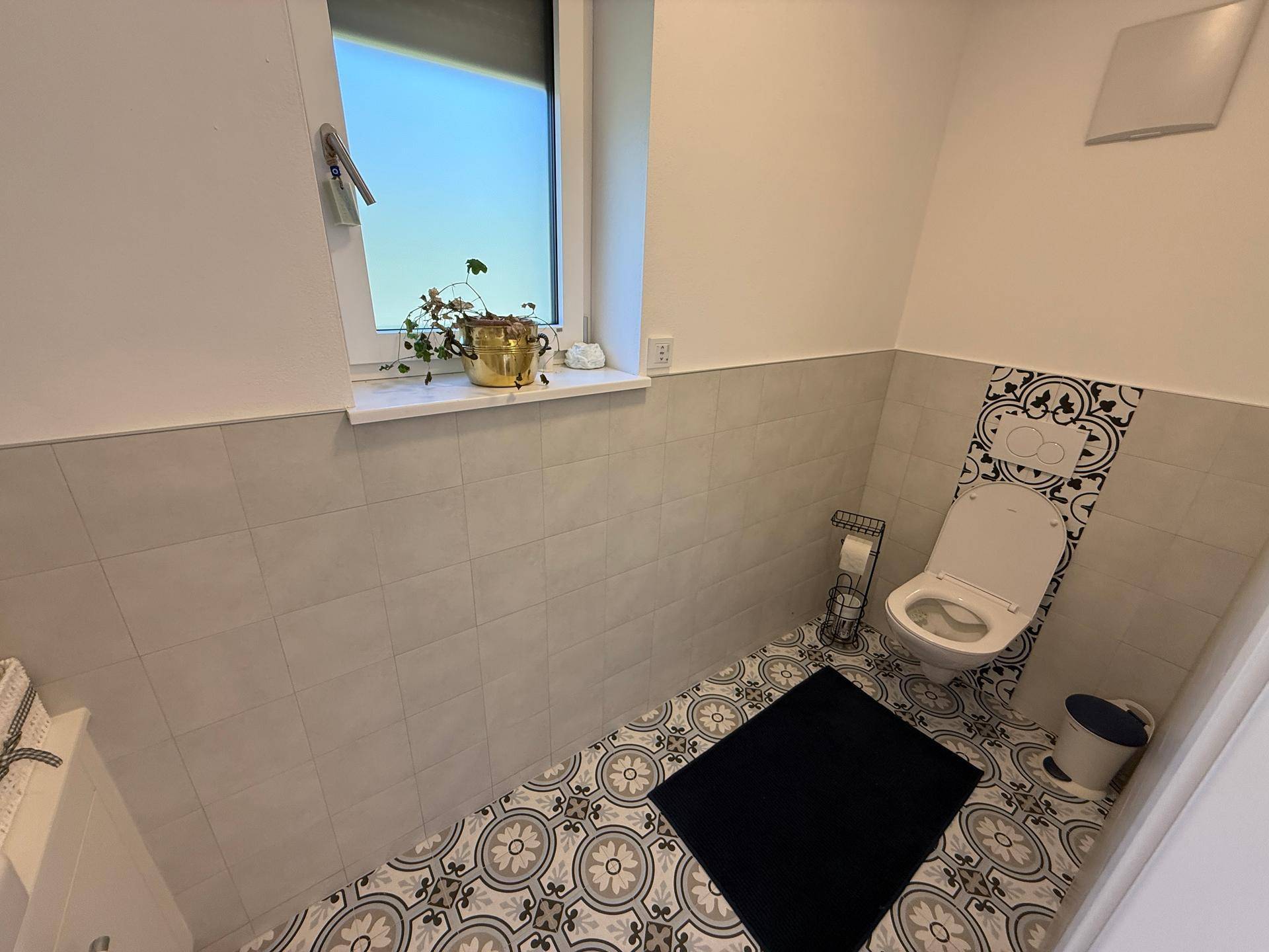 Modernes Gäste-WC mit dekorativen Fliesen, Fenster und wandmontierter Toilette.