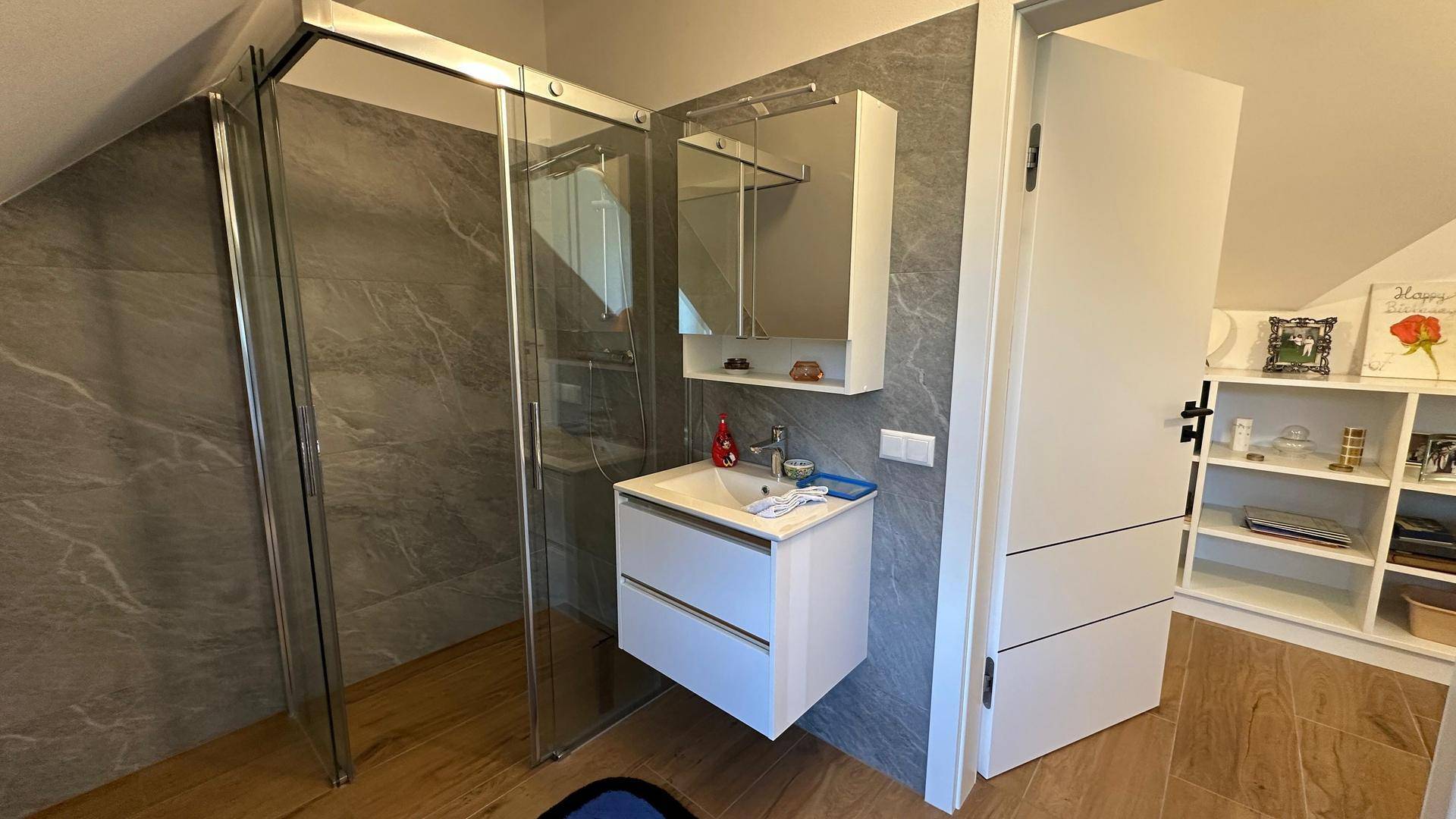 Modernes Badezimmer im Dachgeschoss mit Dusche, Waschtisch und grauen Fliesen.