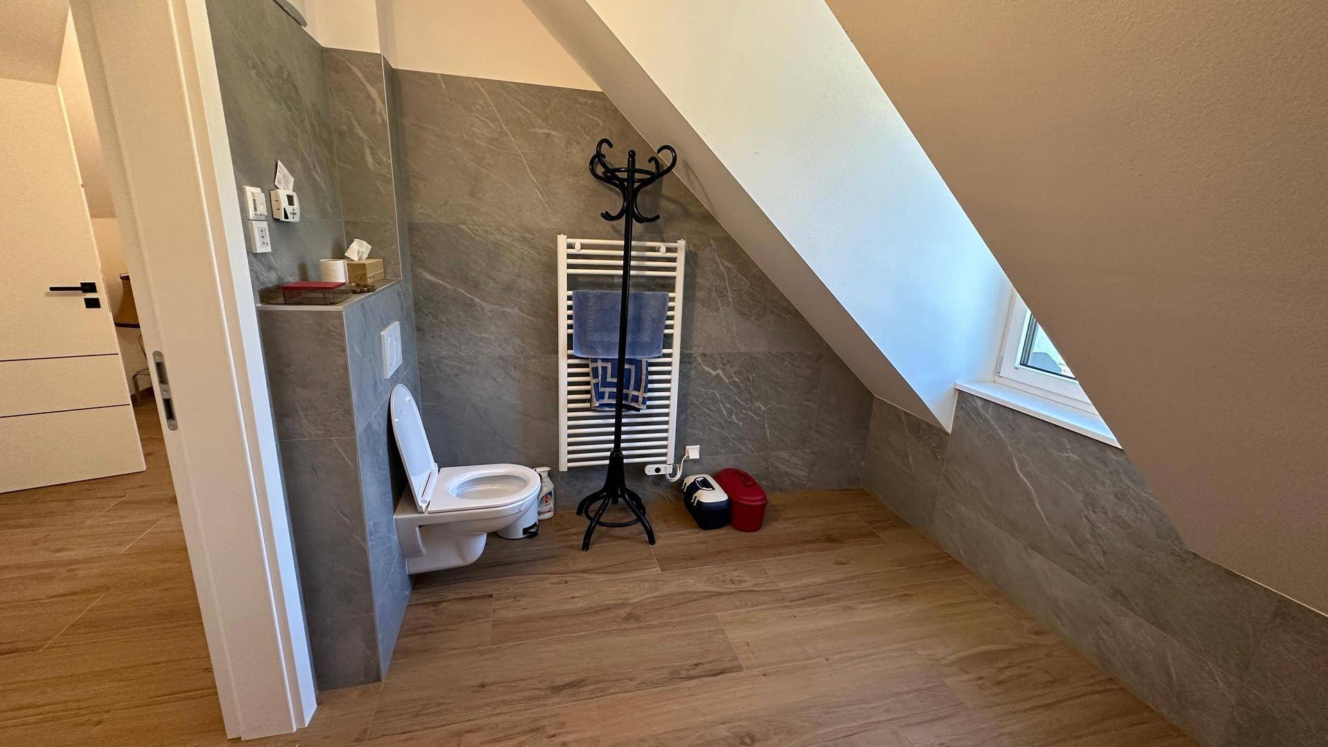 Modernes WC im Dachgeschoss mit Wand-WC, grauen Fliesen und beheiztem Handtuchhalter.