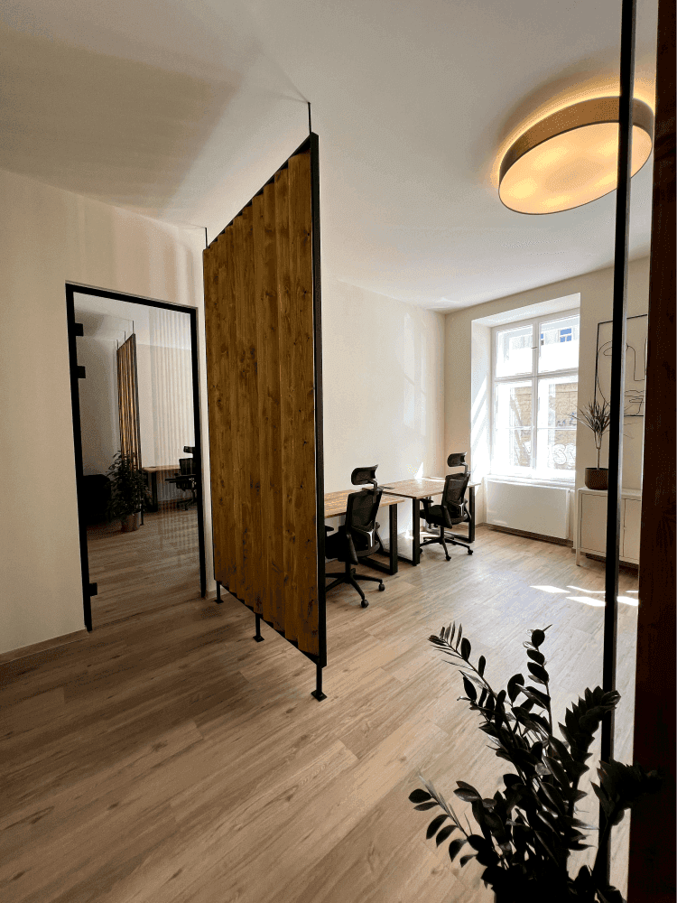 Heller Büroraum mit Holzboden und modernen Arbeitsplätzen, durch eine Holztrennwand und eine Glastür zugänglich.