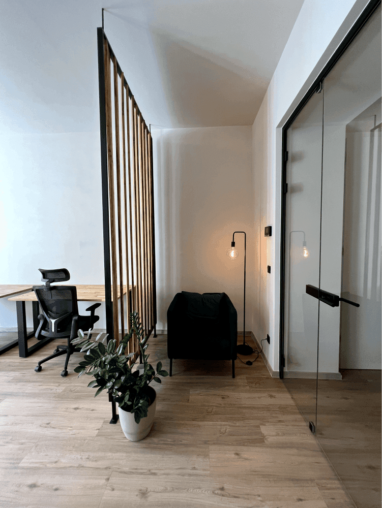 Eingangsbereich des Büros mit einer Holztrennwand, einem bequemen Sessel und einer Stehlampe, die eine einladende Atmosphäre schafft.