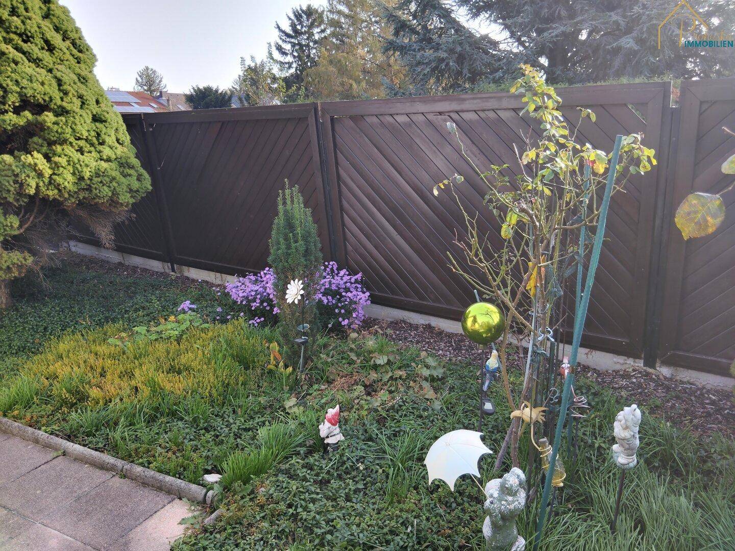 Großer, gepflegter Garten mit Rasenfläche, jungen Bäumen und einem Holzpavillon.
