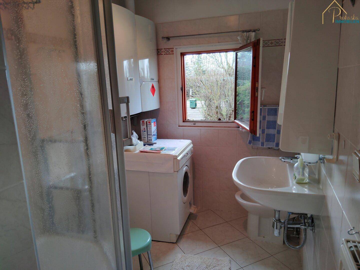 Helles Badezimmer mit Dusche, Waschbecken, WC und Fenster zum Garten.