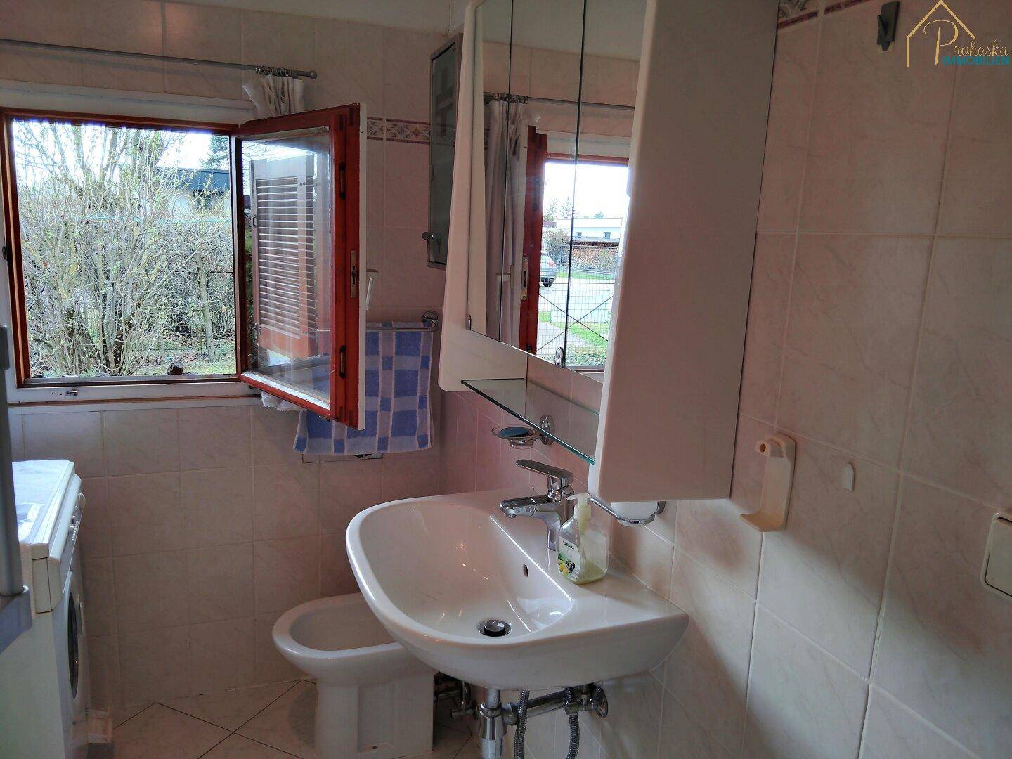 Badezimmer mit Waschbecken, Spiegelschrank, WC und geöffnetem Fenster.