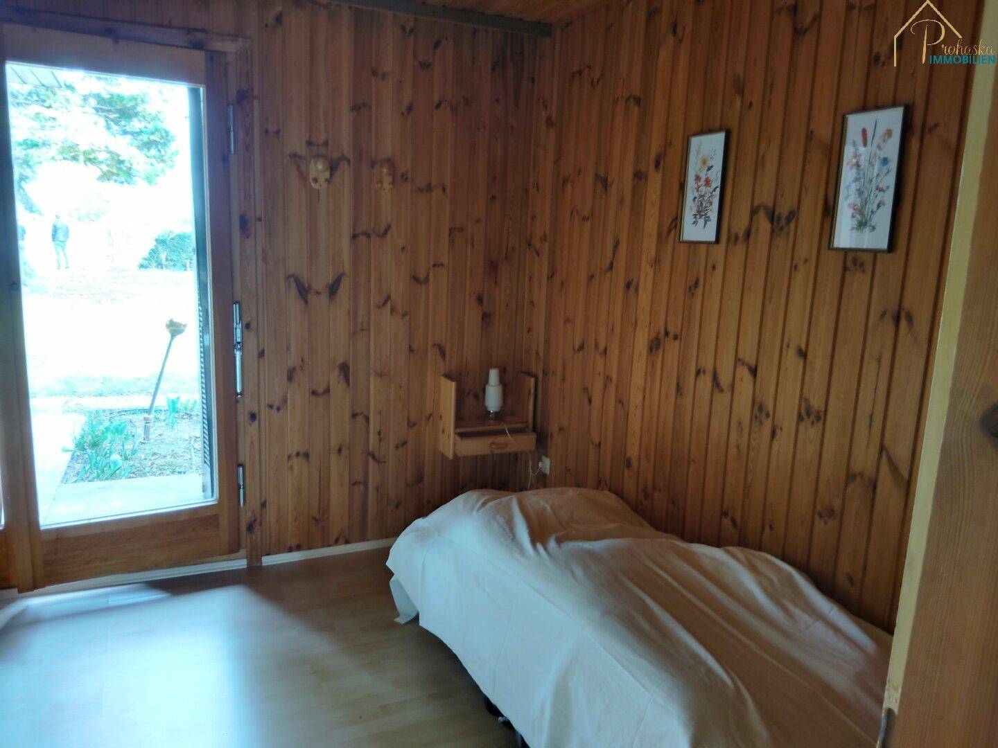 Schlafzimmer mit Einzelbett, Holzvertäfelung und Tür zum Garten.