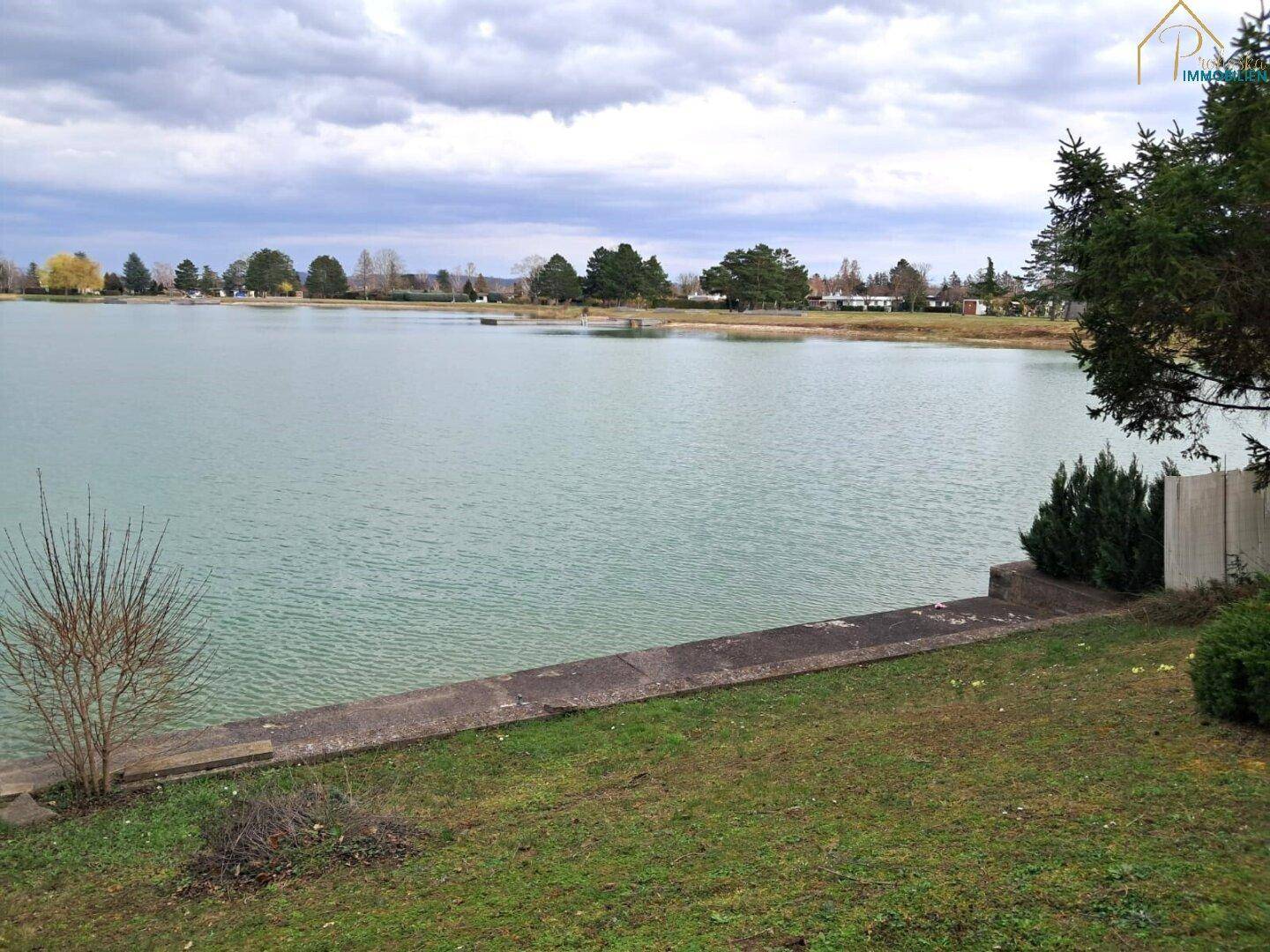 Weitläufiger Blick auf einen ruhigen See unter bewölktem Himmel.