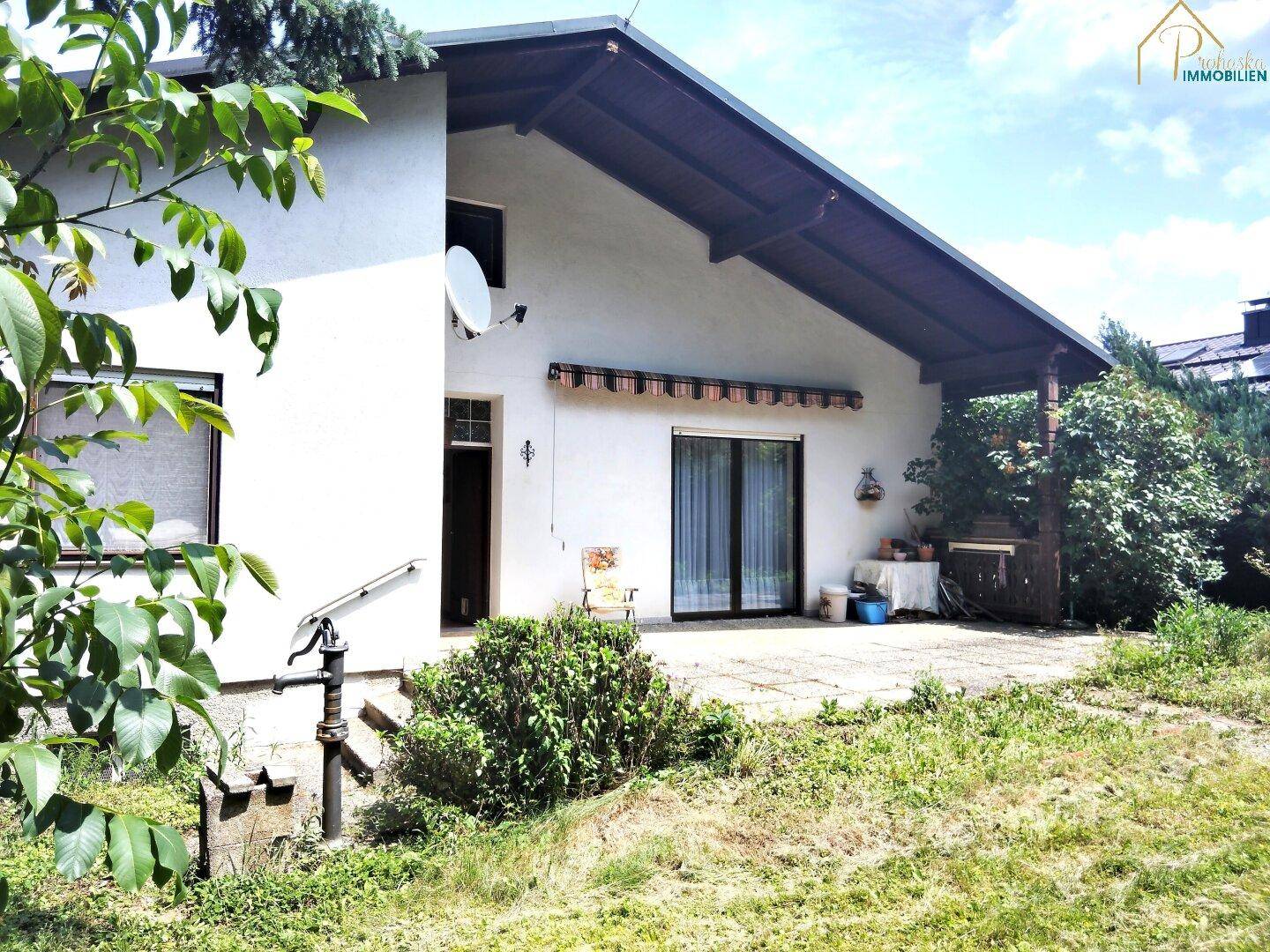 Hausfassade mit überdachter Terrasse, Markise und Zugang zum Garten.
