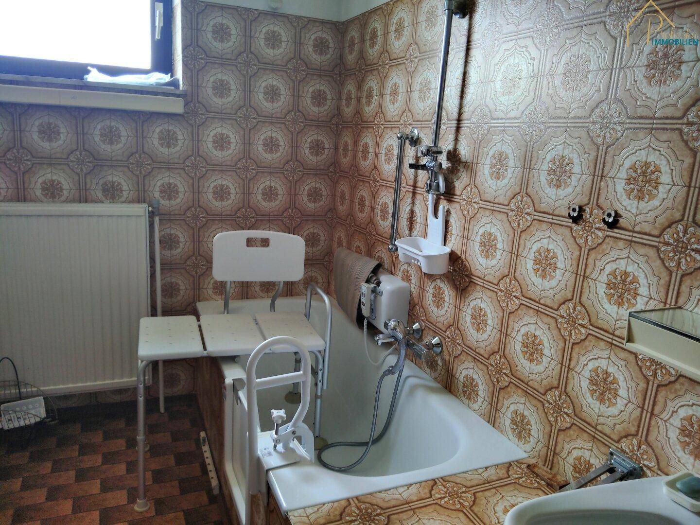 Badezimmer mit Badewanne, gemusterten Fliesen und Hilfsmitteln für Barrierefreiheit.