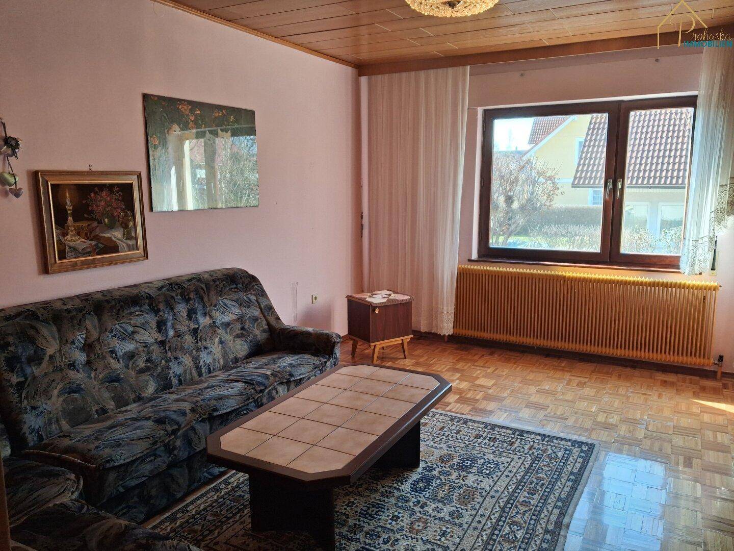 Wohnzimmer mit Sofa, Couchtisch, Parkettboden und großem Fenster.