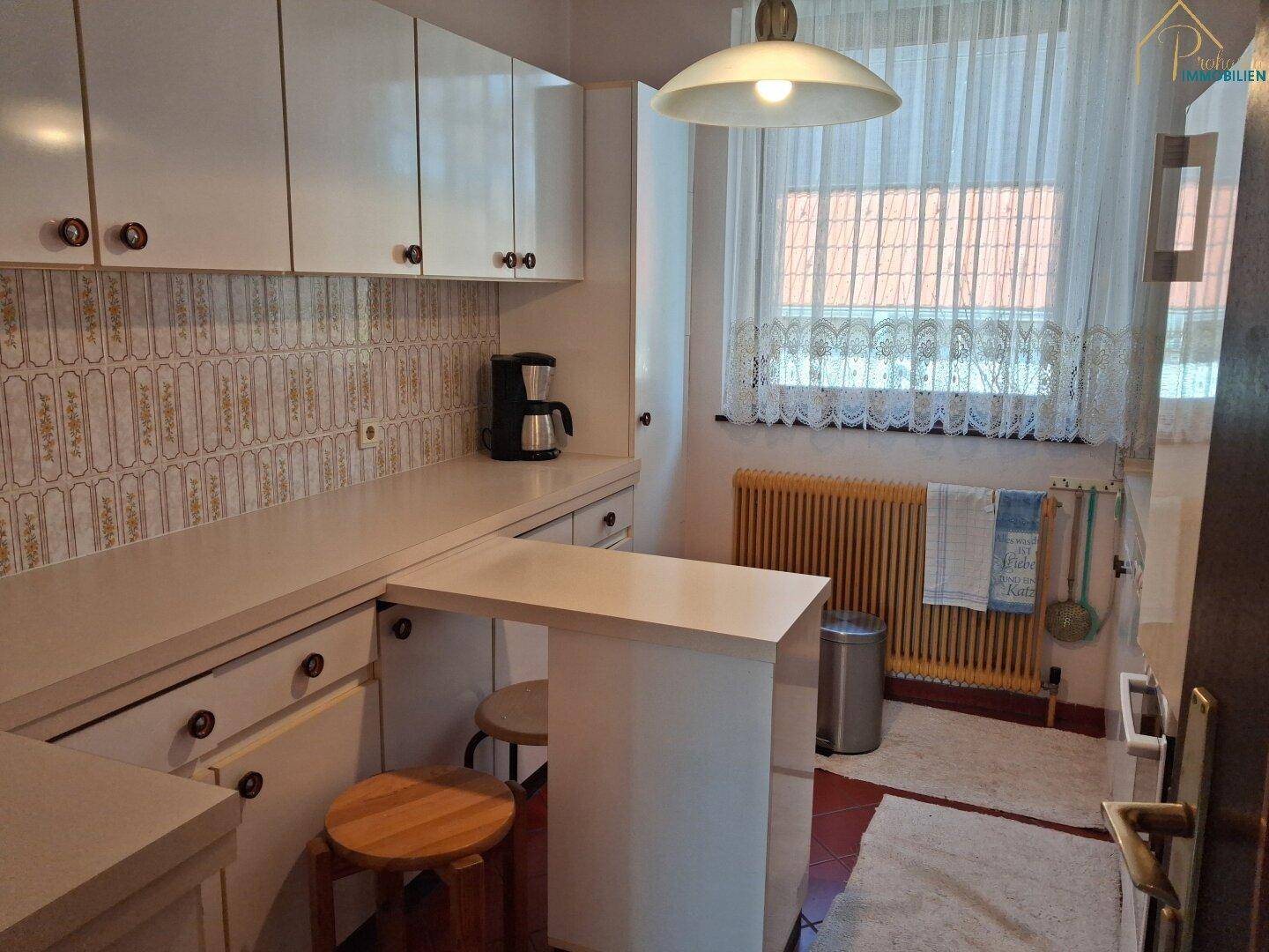 Helle Küche mit weißen Schränken, kleiner Frühstücksbar und Fenster.