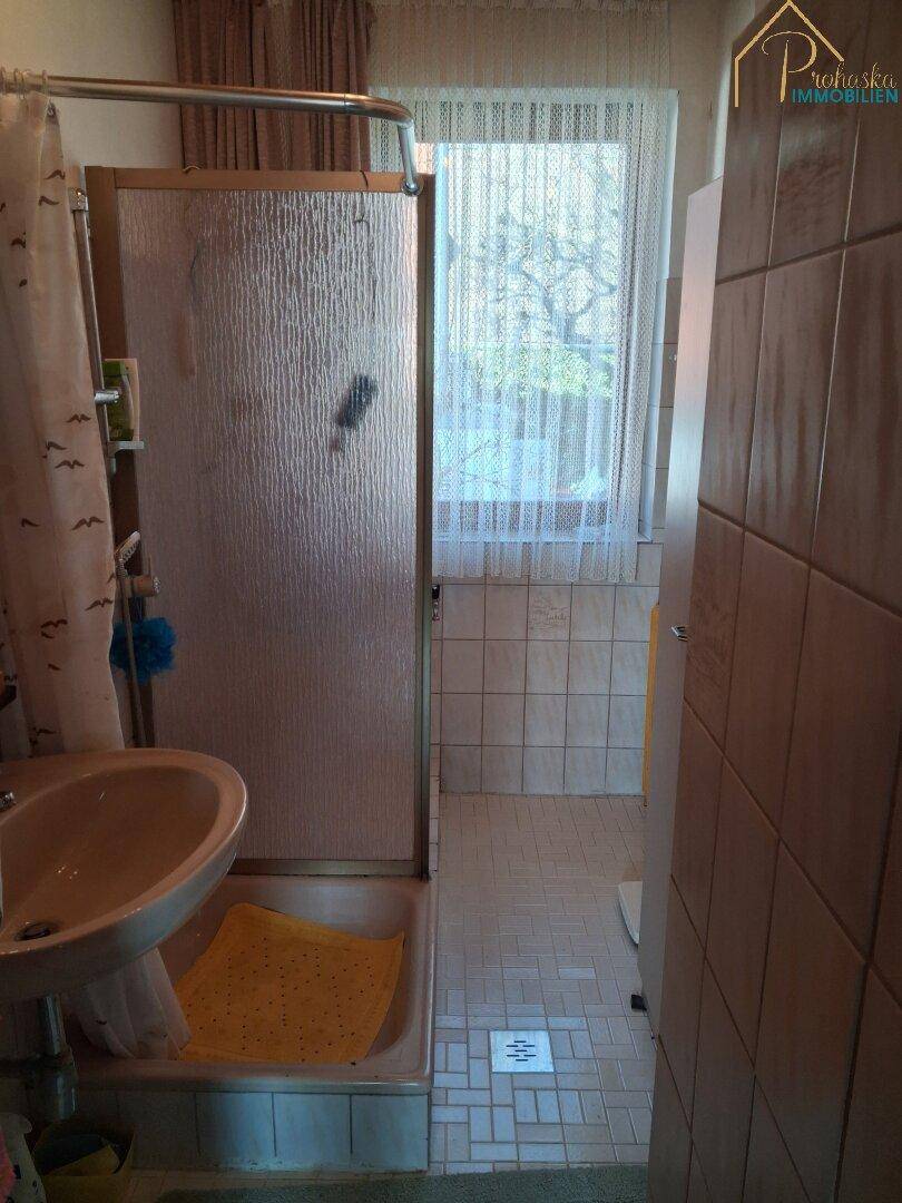 Badezimmer mit Dusche, Waschbecken und Fliesen im 80er-Jahre-Stil.