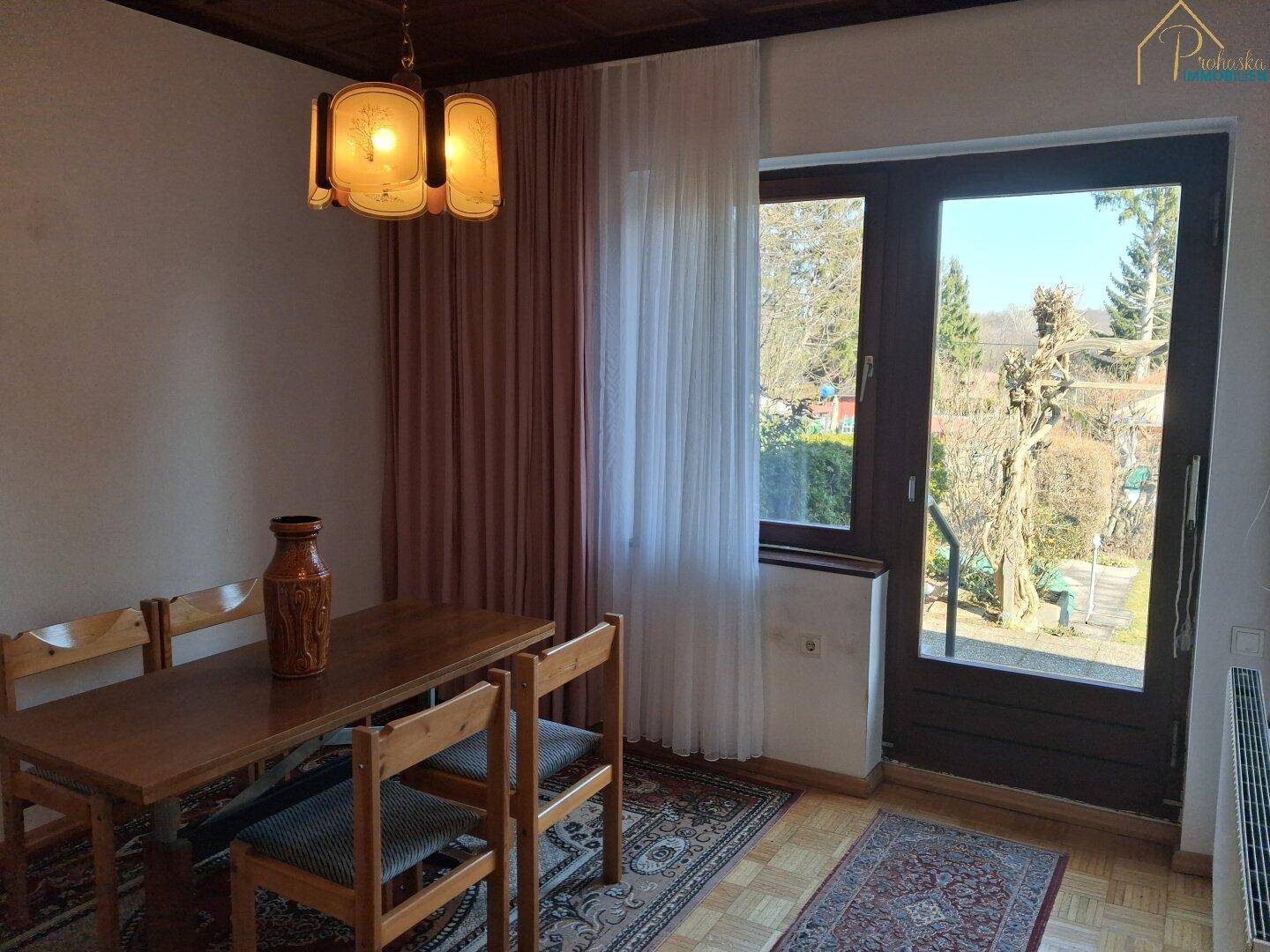 Esszimmer mit Holztisch, Stühlen und Zugang zum Garten.