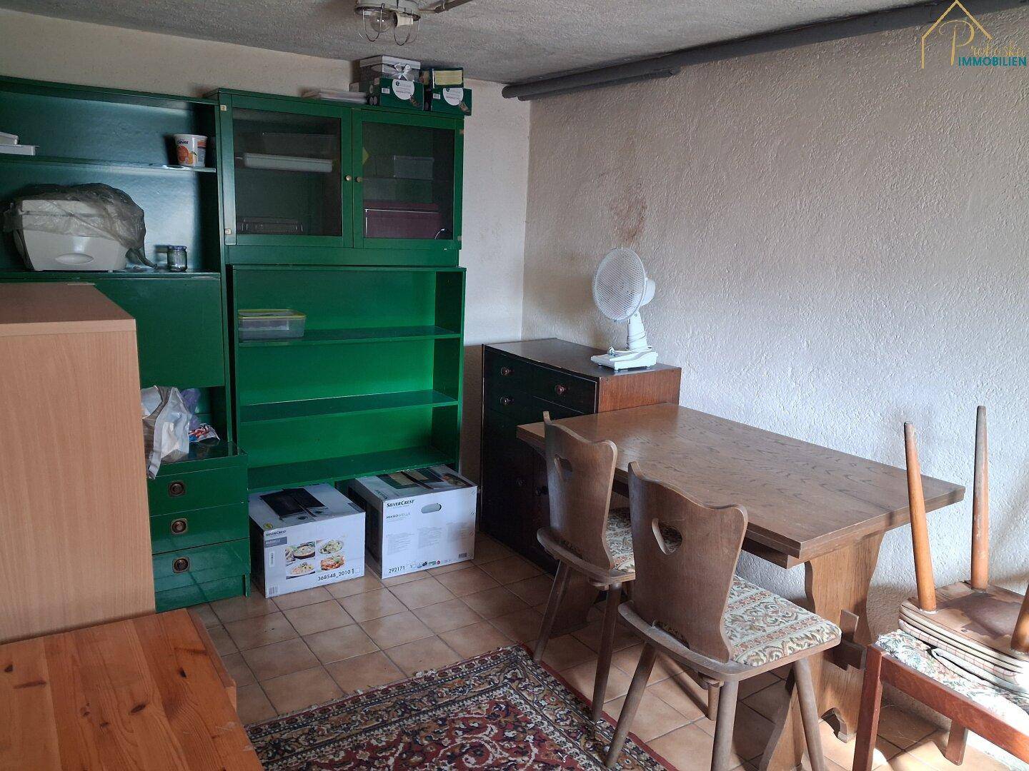 Kellerraum mit Tisch, Stühlen, Regal und Fliesenboden.
