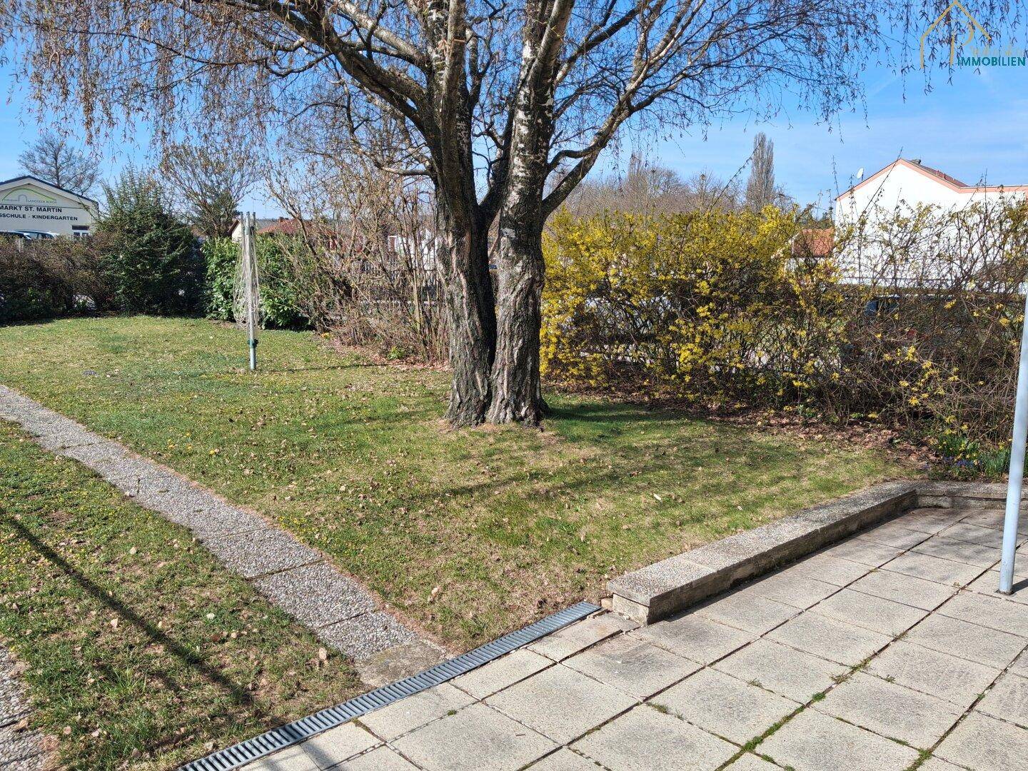 Gepflegter Gartenbereich mit Rasenfläche, gepflastertem Weg und Bäumen.