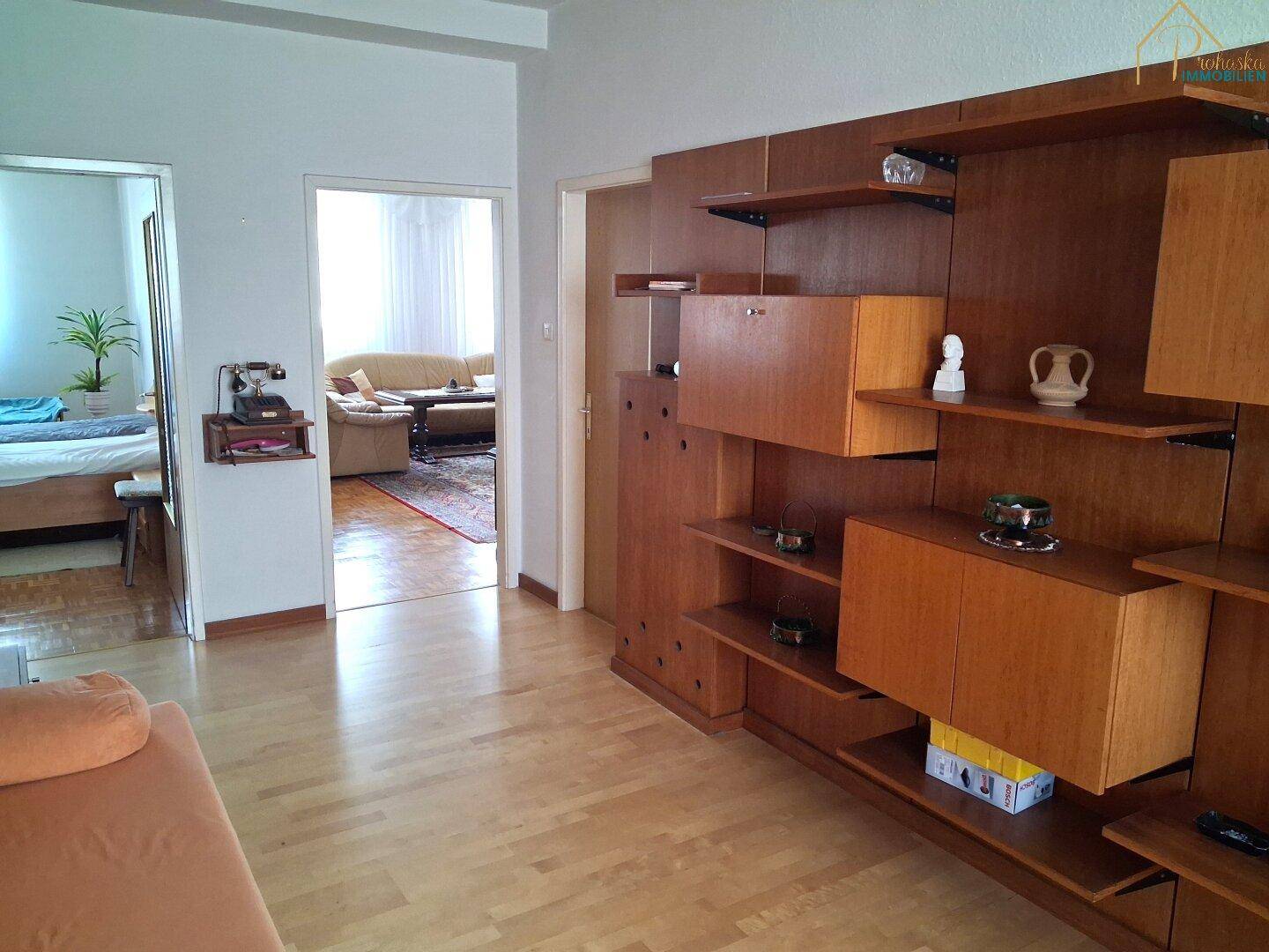 Zimmer mit Holzregalsystem und Durchgang zu einem weiteren Wohnbereich.