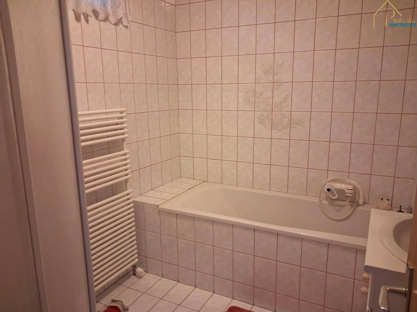 Badezimmer mit Badewanne, beheiztem Handtuchhalter und hellen Fliesen.