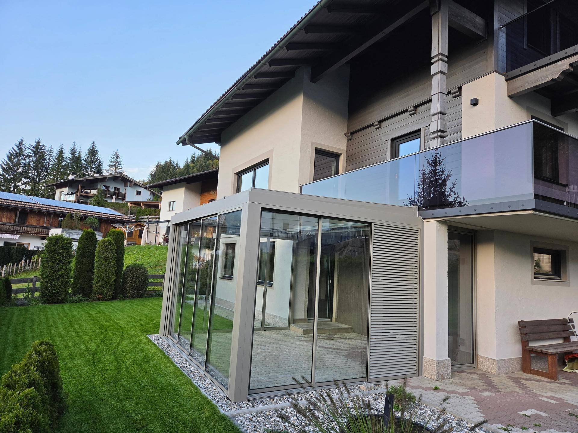 Moderne Glaserweiterung als Wintergarten mit Zugang zum Garten und Balkon darüber.
