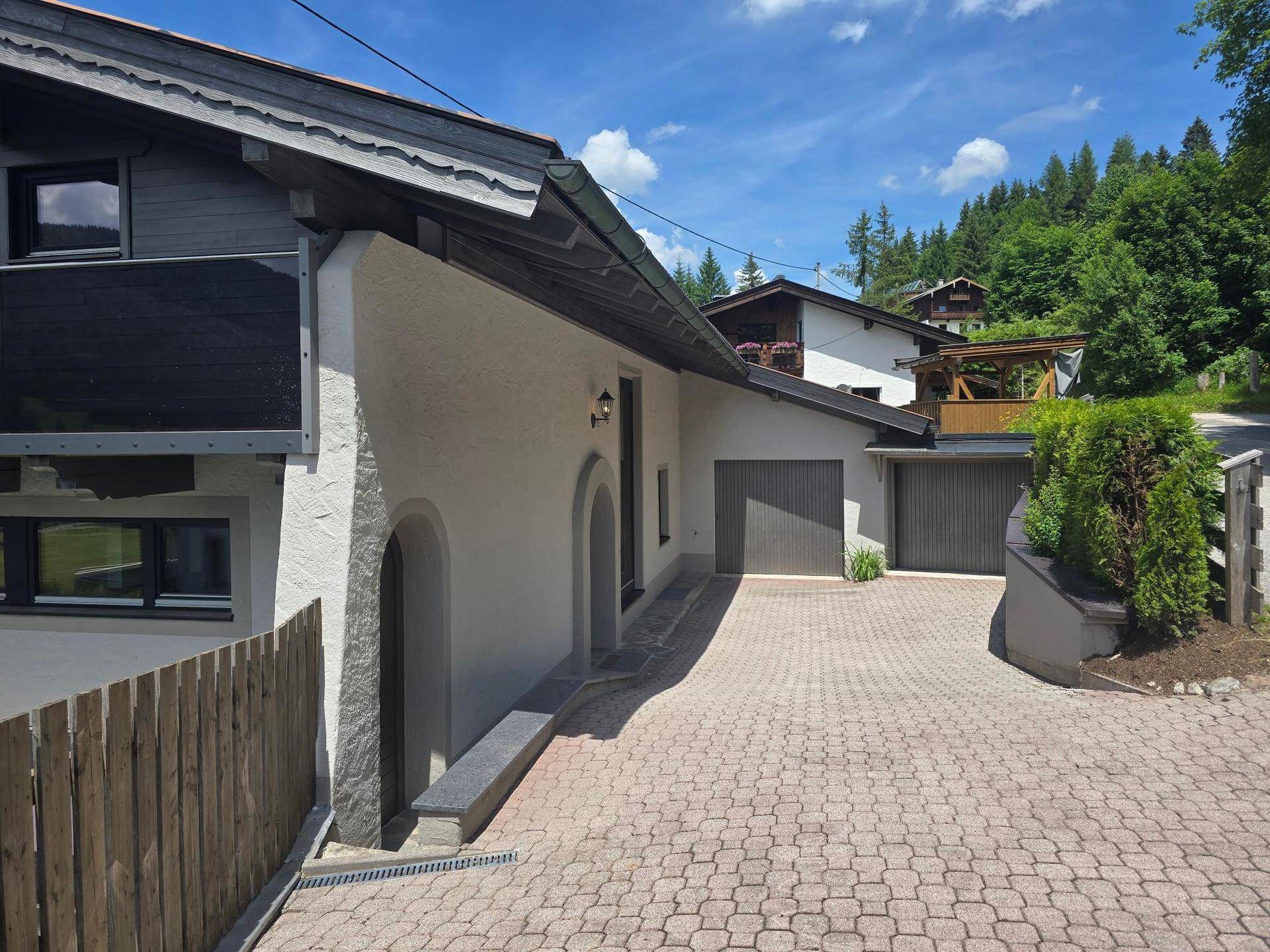 Seitenansicht des Hauses mit gepflasterter Auffahrt und zwei Garagen.