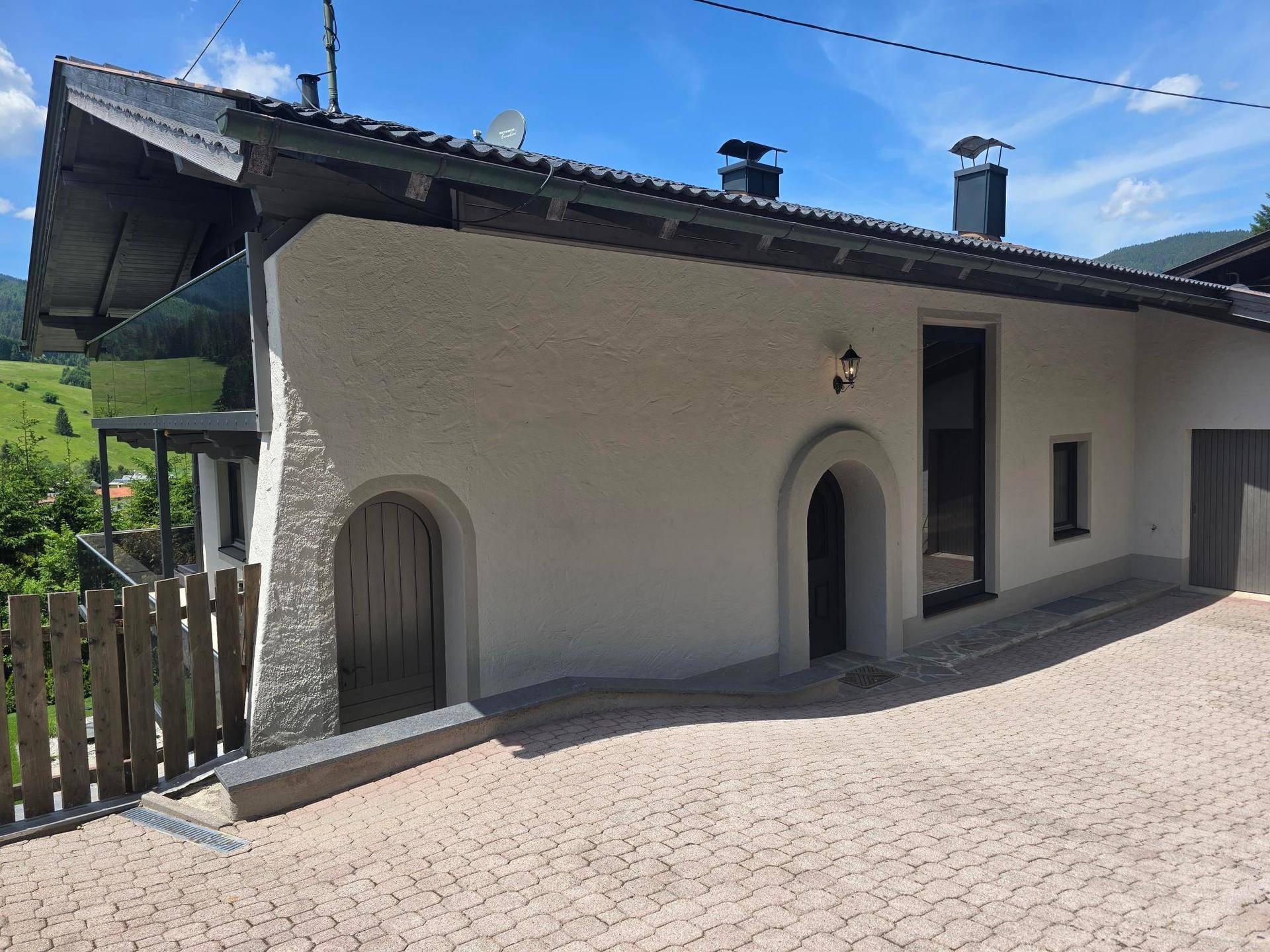 Eingangsbereich des Hauses mit gewölbten Türen und gepflasterter Zufahrt.