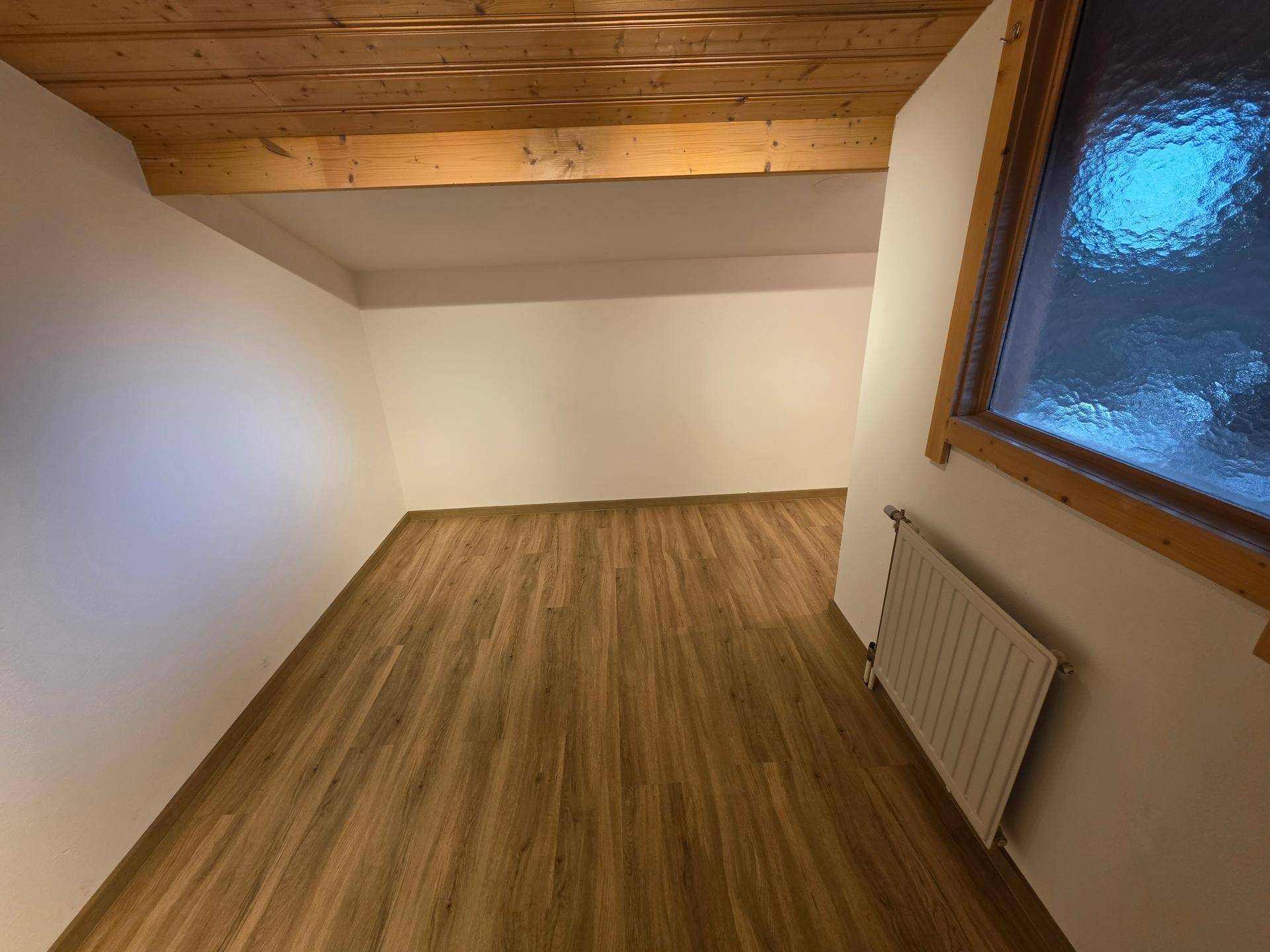 Dachgeschosszimmer mit Holzbalken, schräger Decke und Laminatboden.