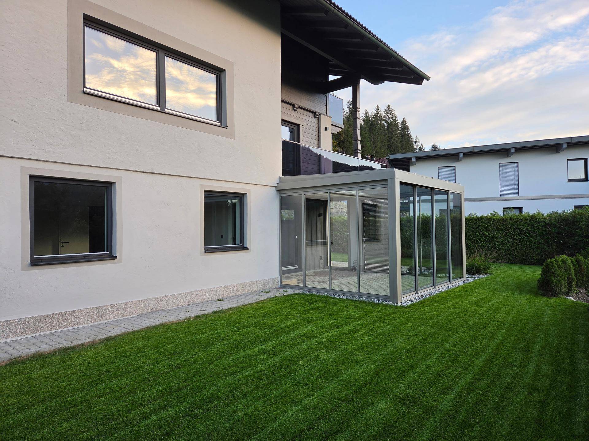 Gepflegter Rasenbereich neben dem Haus mit moderner Glaserweiterung und großen Fenstern.