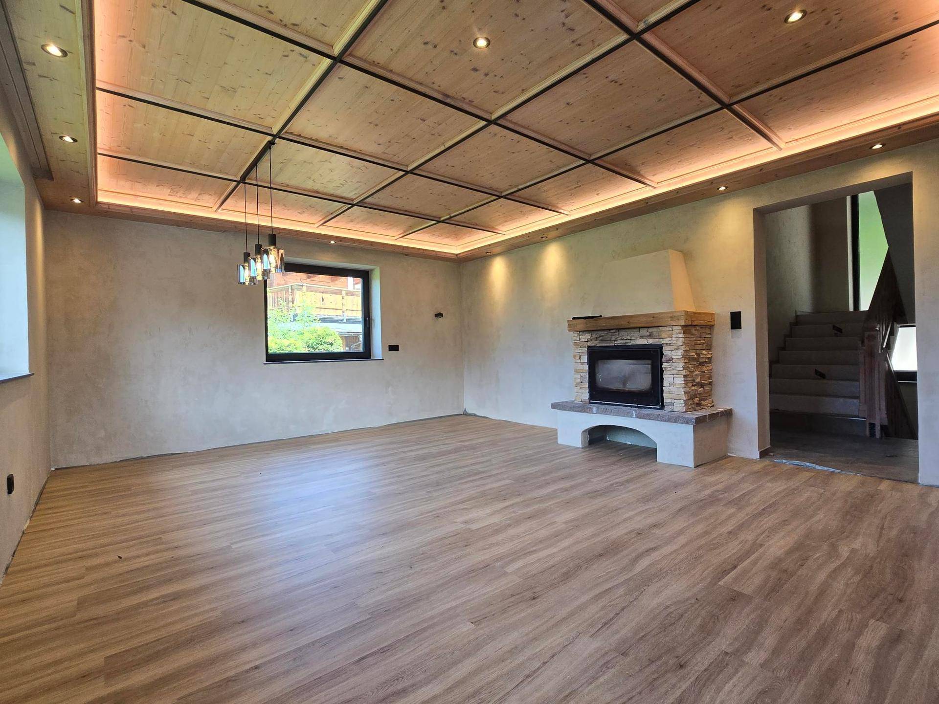 Gemütliches Wohnzimmer mit Kamin, Holzboden und Kassettendecke, bereit für Einrichtung.
