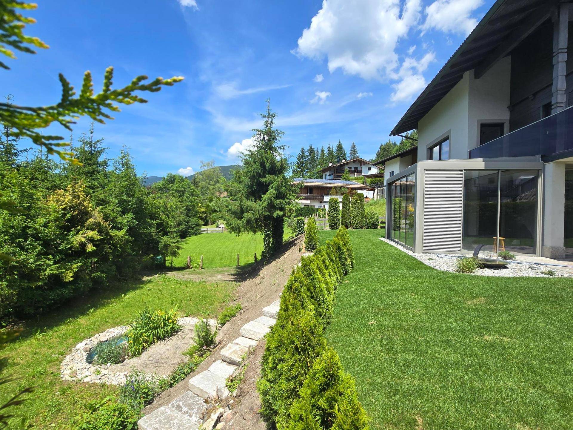 Gepflegter Gartenbereich mit Rasenfläche, Bäumen und Blick auf die umliegende Natur.