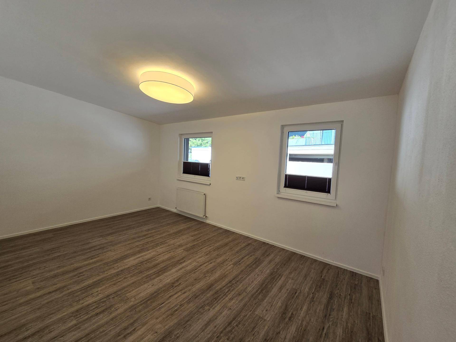 Helles Schlafzimmer mit zwei Fenstern und Laminatboden, ideal für individuelle Gestaltung.
