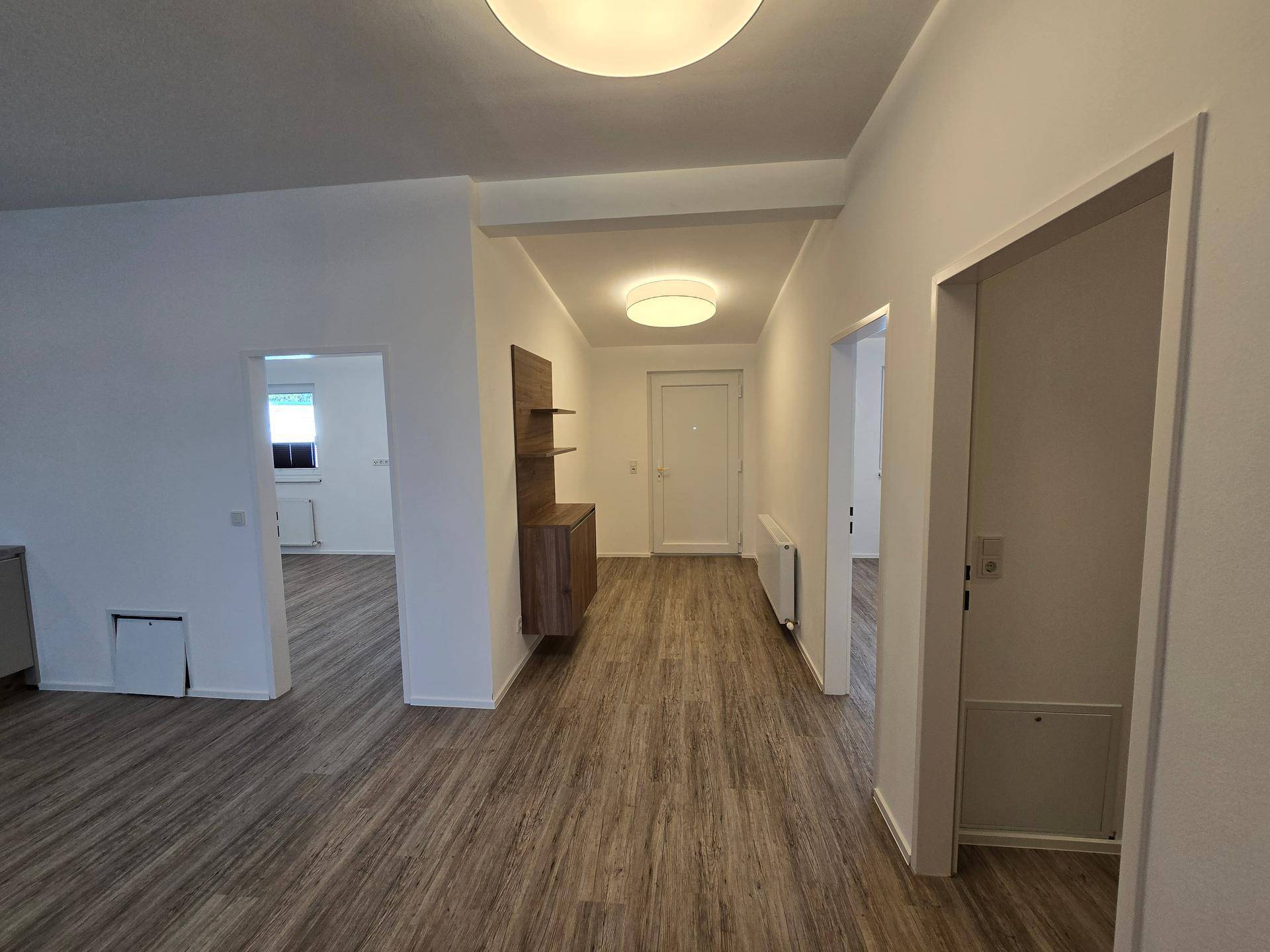 Heller Flur mit Laminatboden und modernem Wandregal, der zu weiteren Räumen führt.