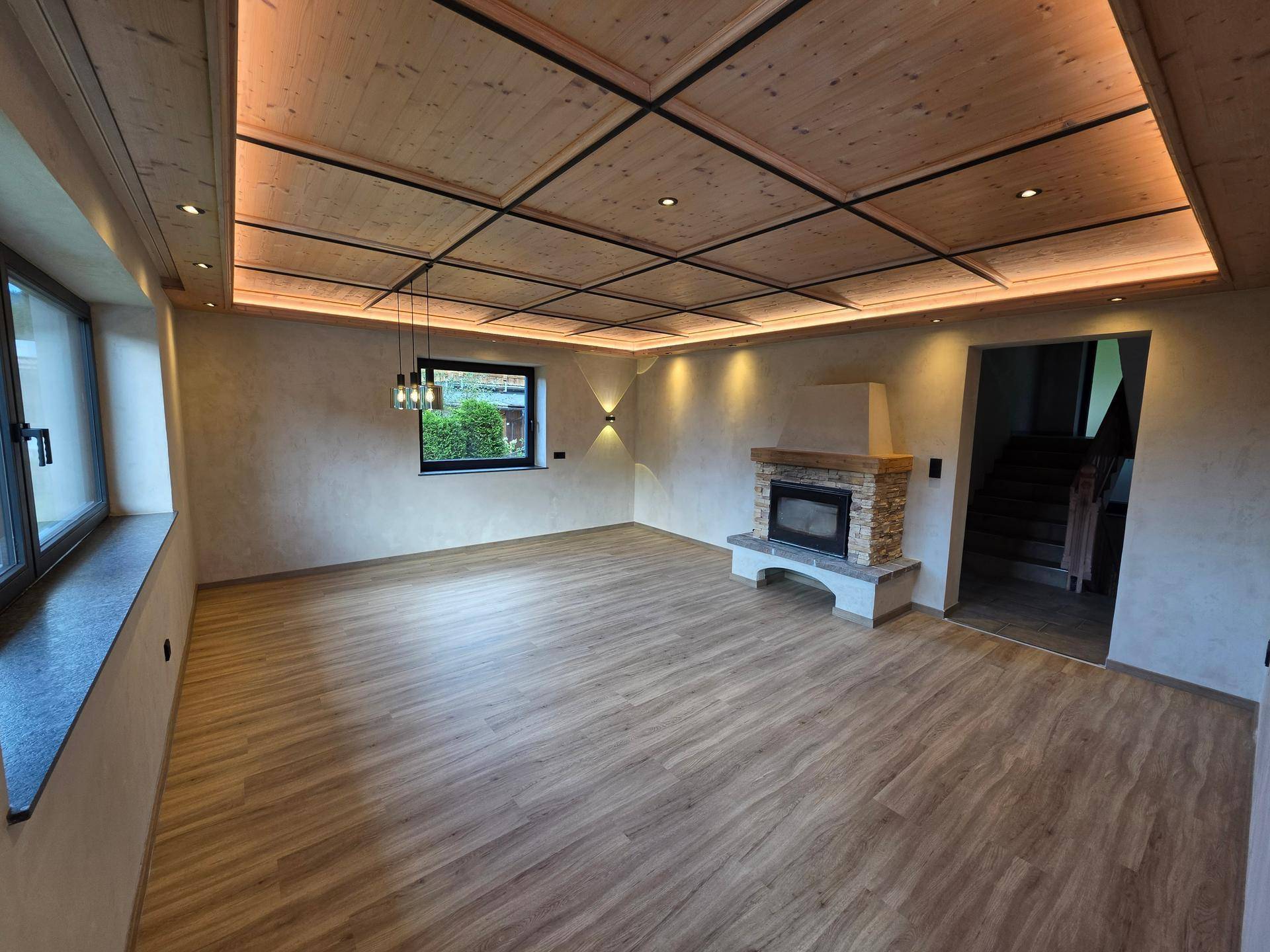 Heller Wohnbereich mit Kamin, Holzkassettendecke und modernem Laminatboden.