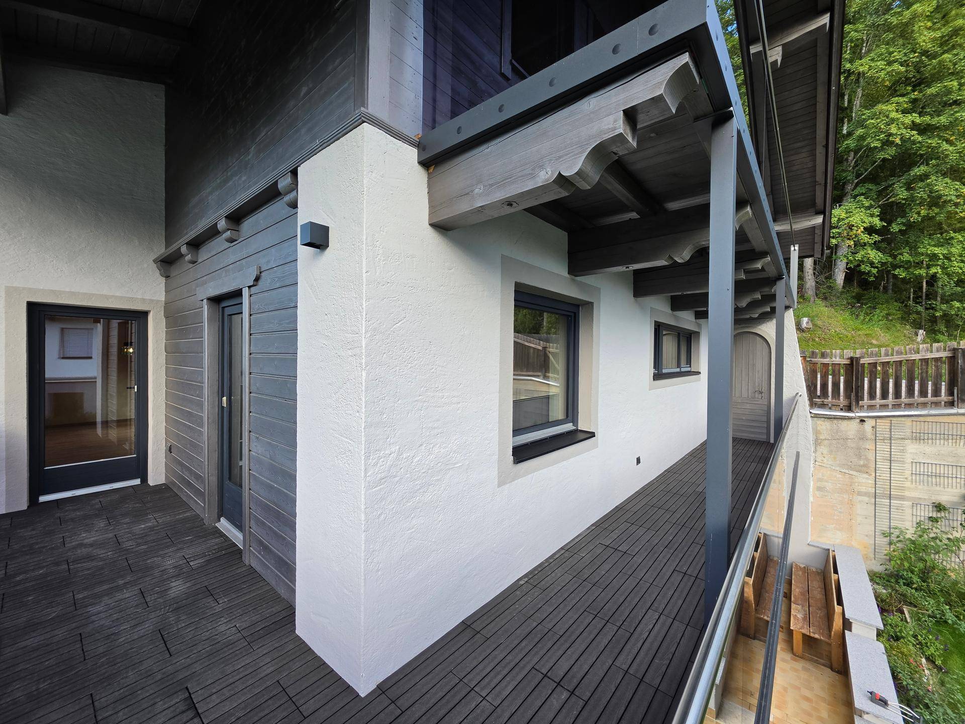 Langer Balkon mit Holzboden und traditionellen Holzelementen, umgeben von Natur.