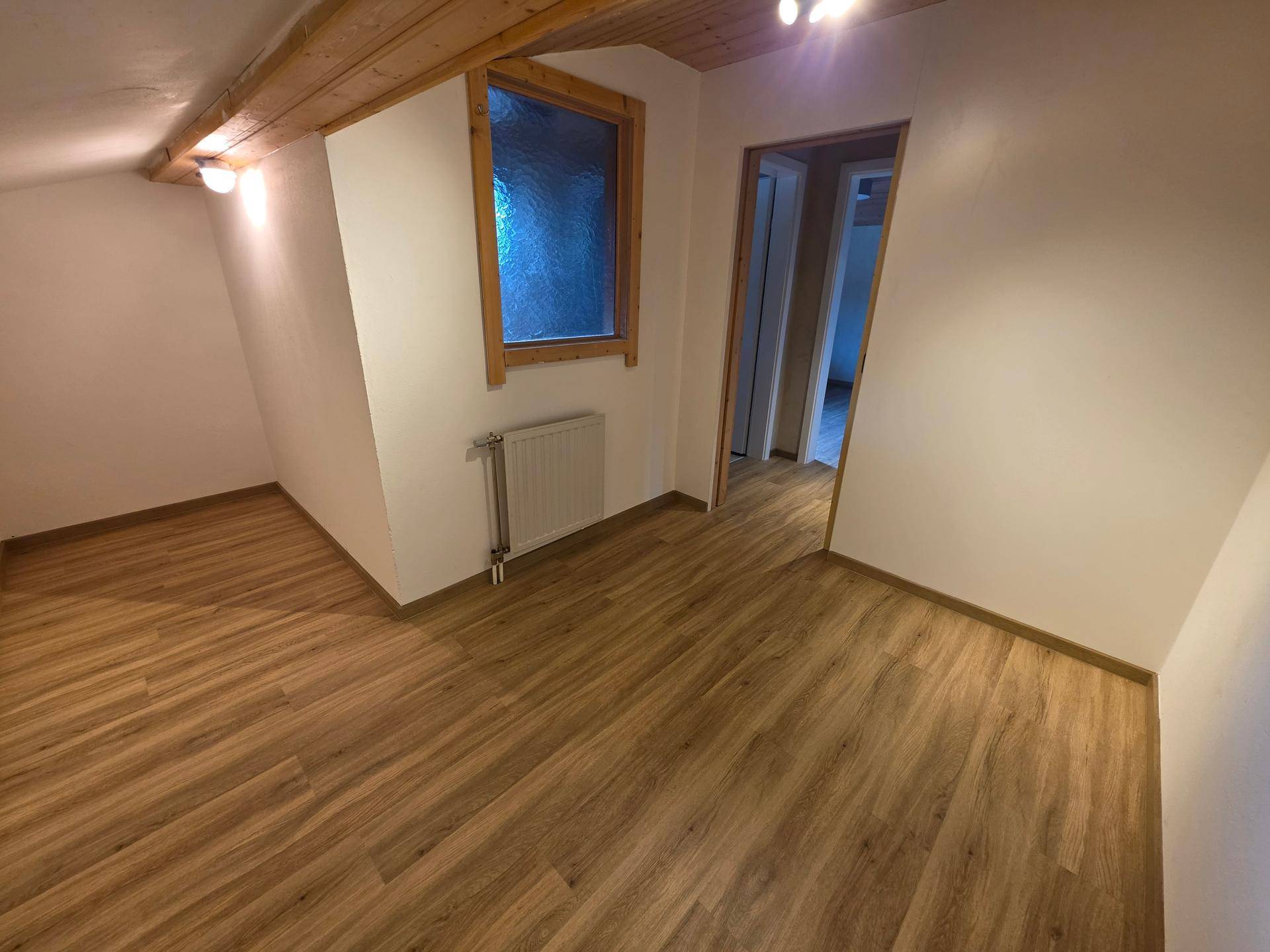 Kleineres Zimmer mit schräger Decke, sichtbaren Holzbalken und Laminatboden.