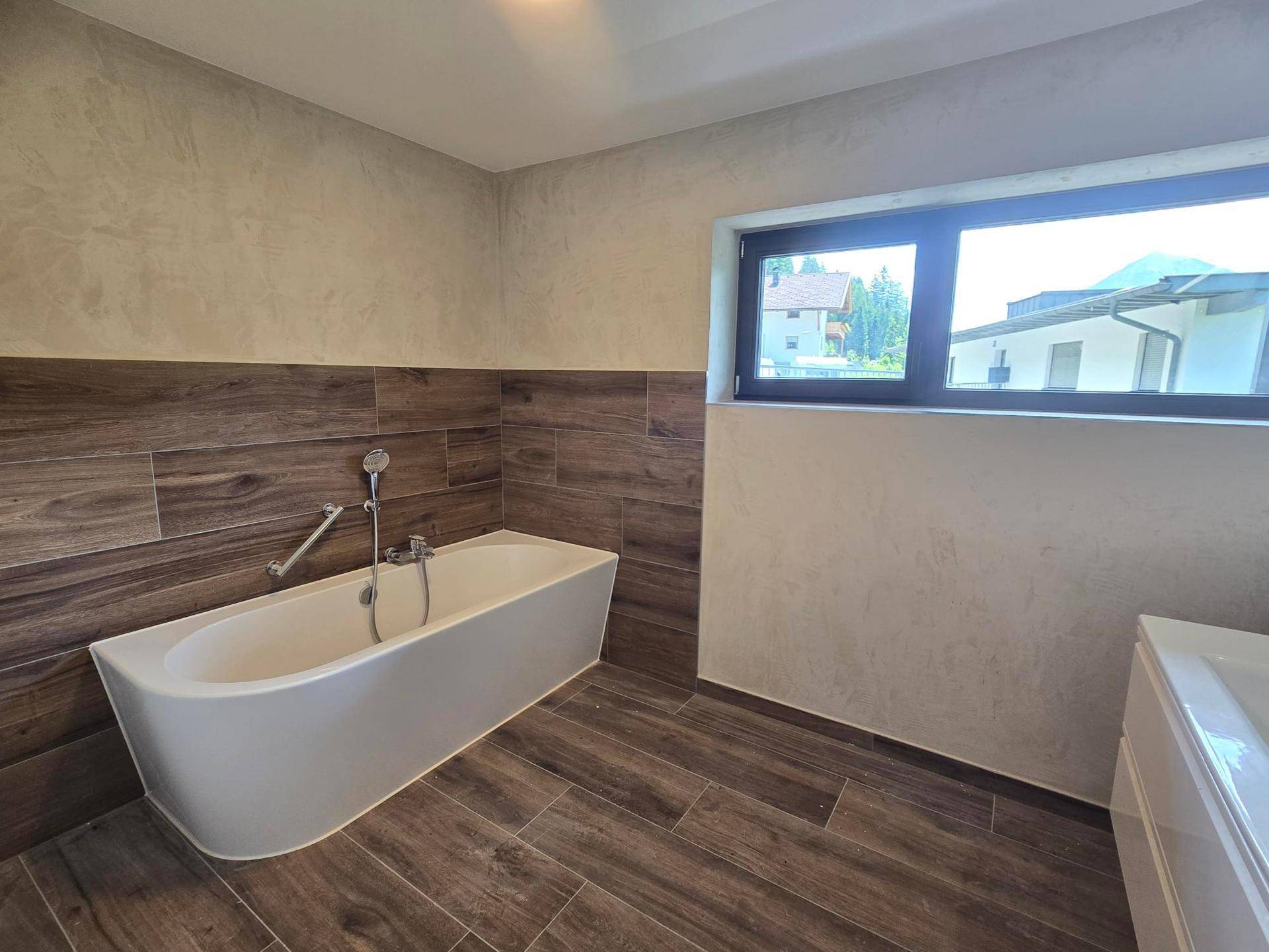 Modernes Badezimmer mit Badewanne, Holzoptikfliesen und Fenster mit Bergblick.