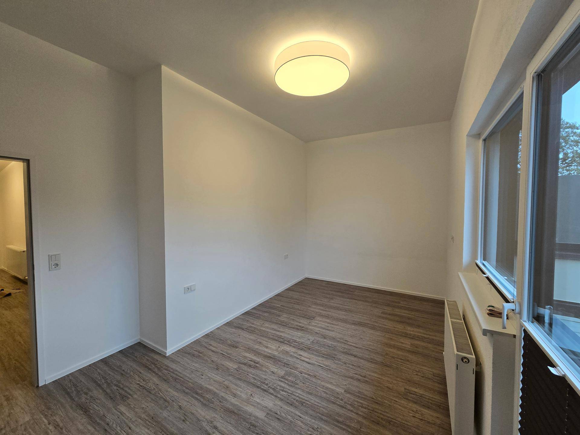 Geräumiges Schlafzimmer mit Laminatboden und großem Fenster, bereit zur Einrichtung.