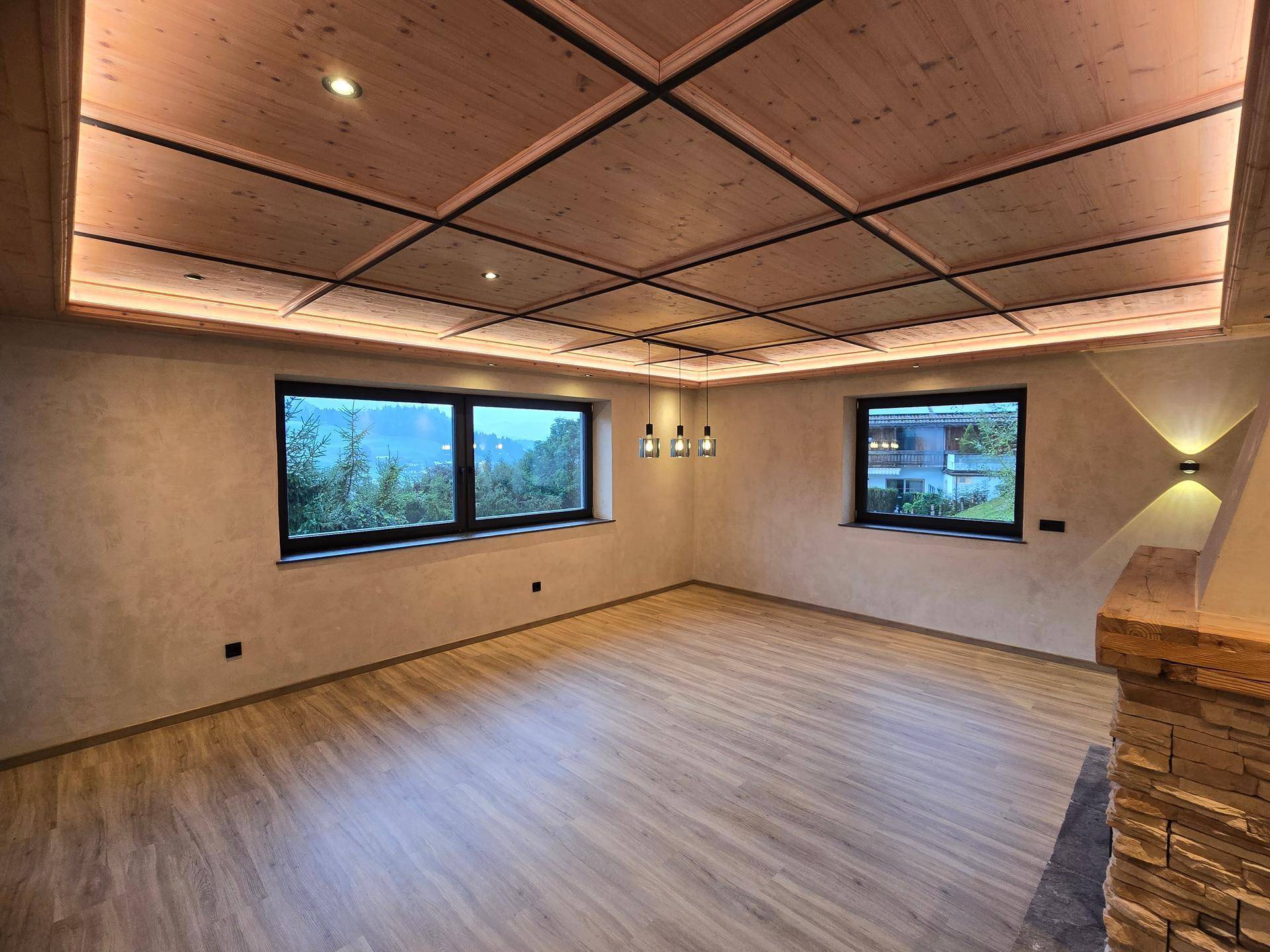 Geräumiger Wohnbereich mit Holzkassettendecke, indirekter Beleuchtung und großen Fenstern.