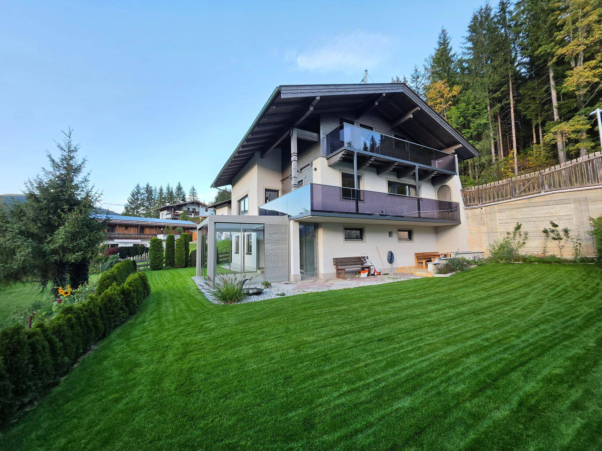 Großzügiger Gartenbereich mit gepflegtem Rasen, moderner Glaserweiterung und Bergblick.