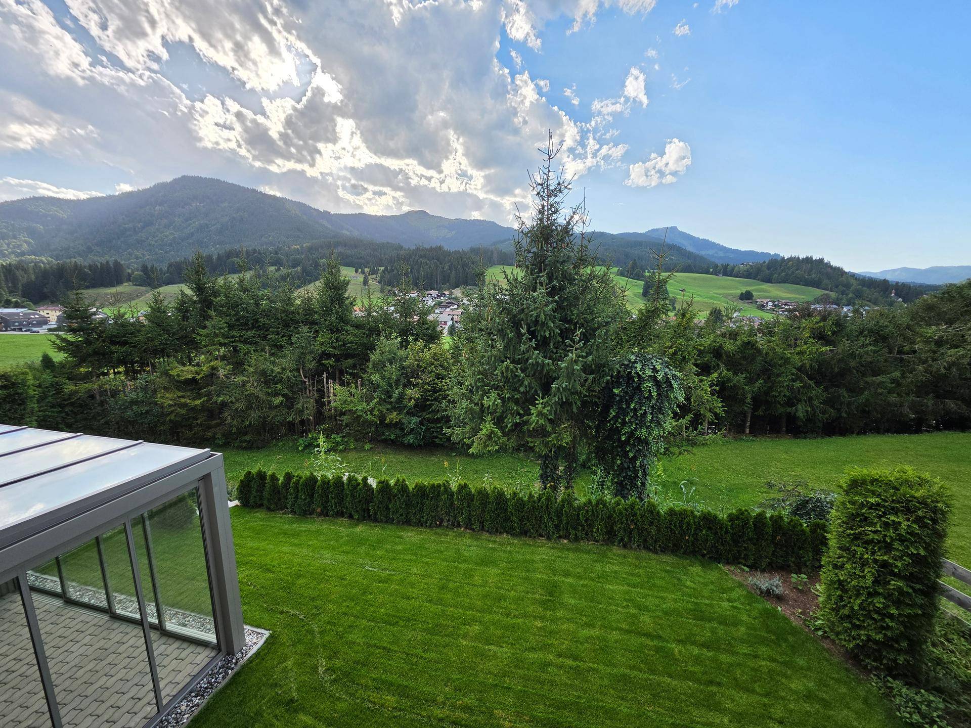 Gepflegter Garten mit Rasenfläche, Hecke und weitem Blick auf die umliegende Berglandschaft.