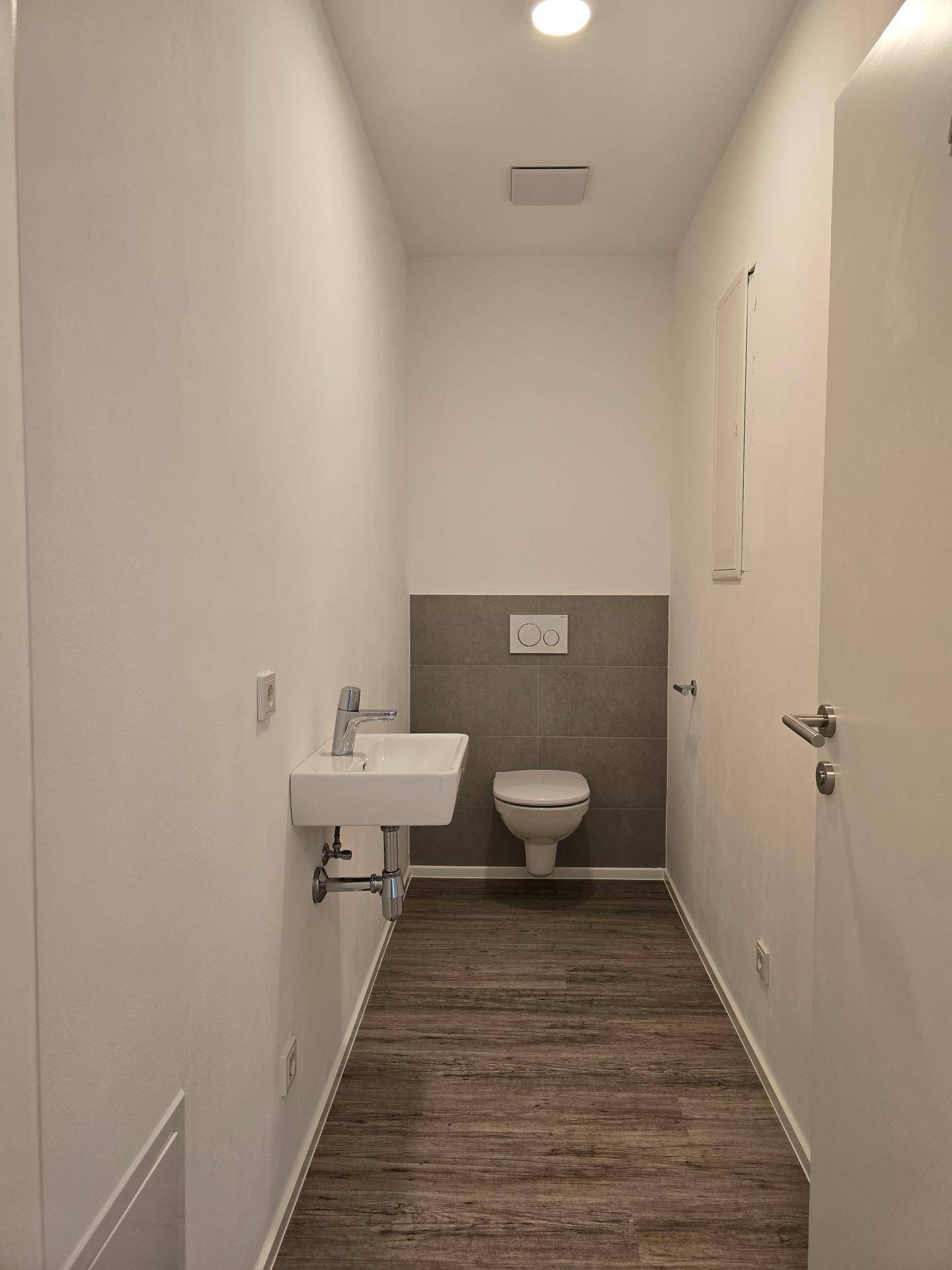 Separates Gäste-WC mit wandhängender Toilette und kleinem Waschbecken.