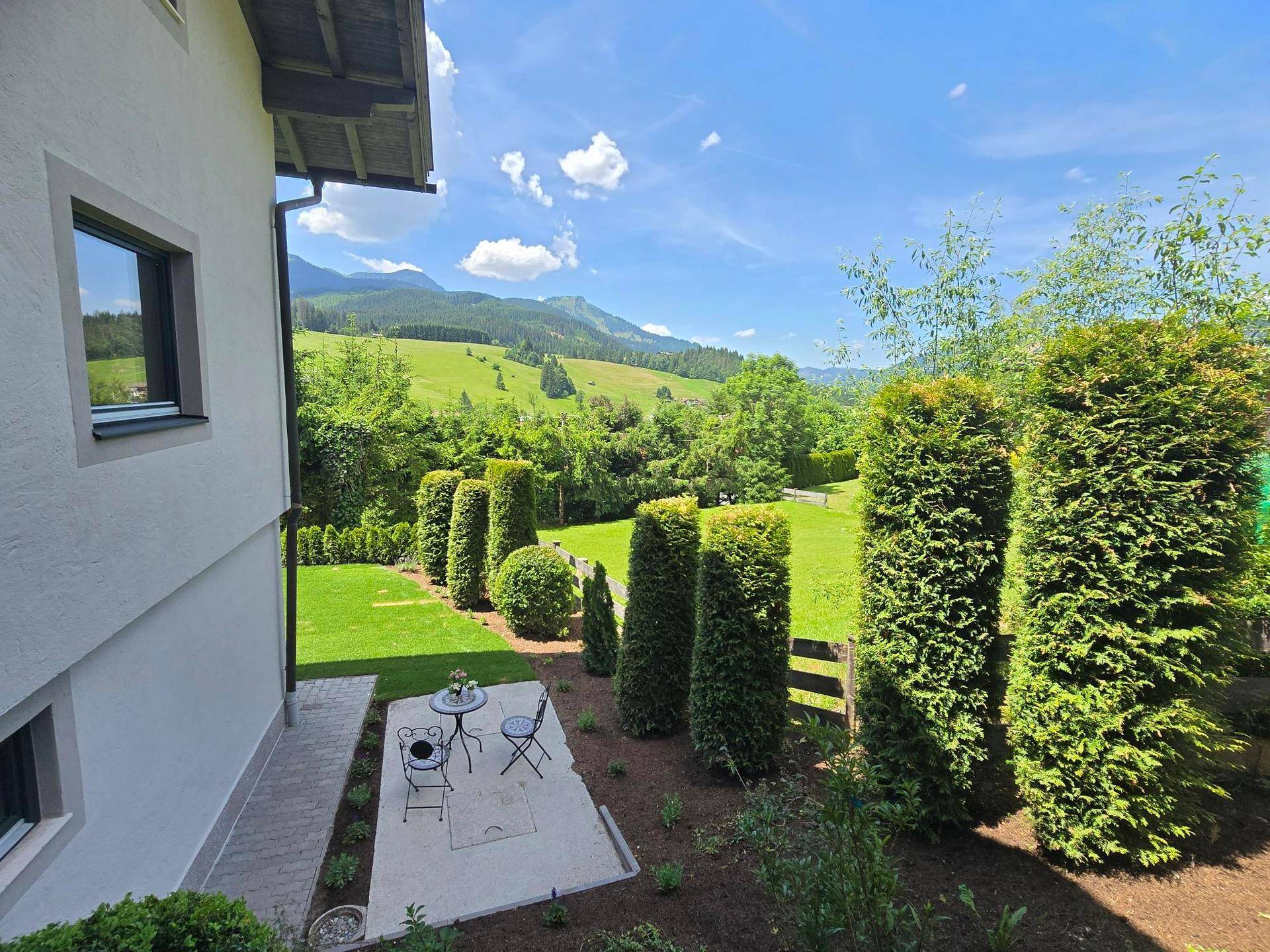 Kleine Terrasse mit Sitzgelegenheiten im Garten und weitem Blick auf die grüne Berglandschaft.