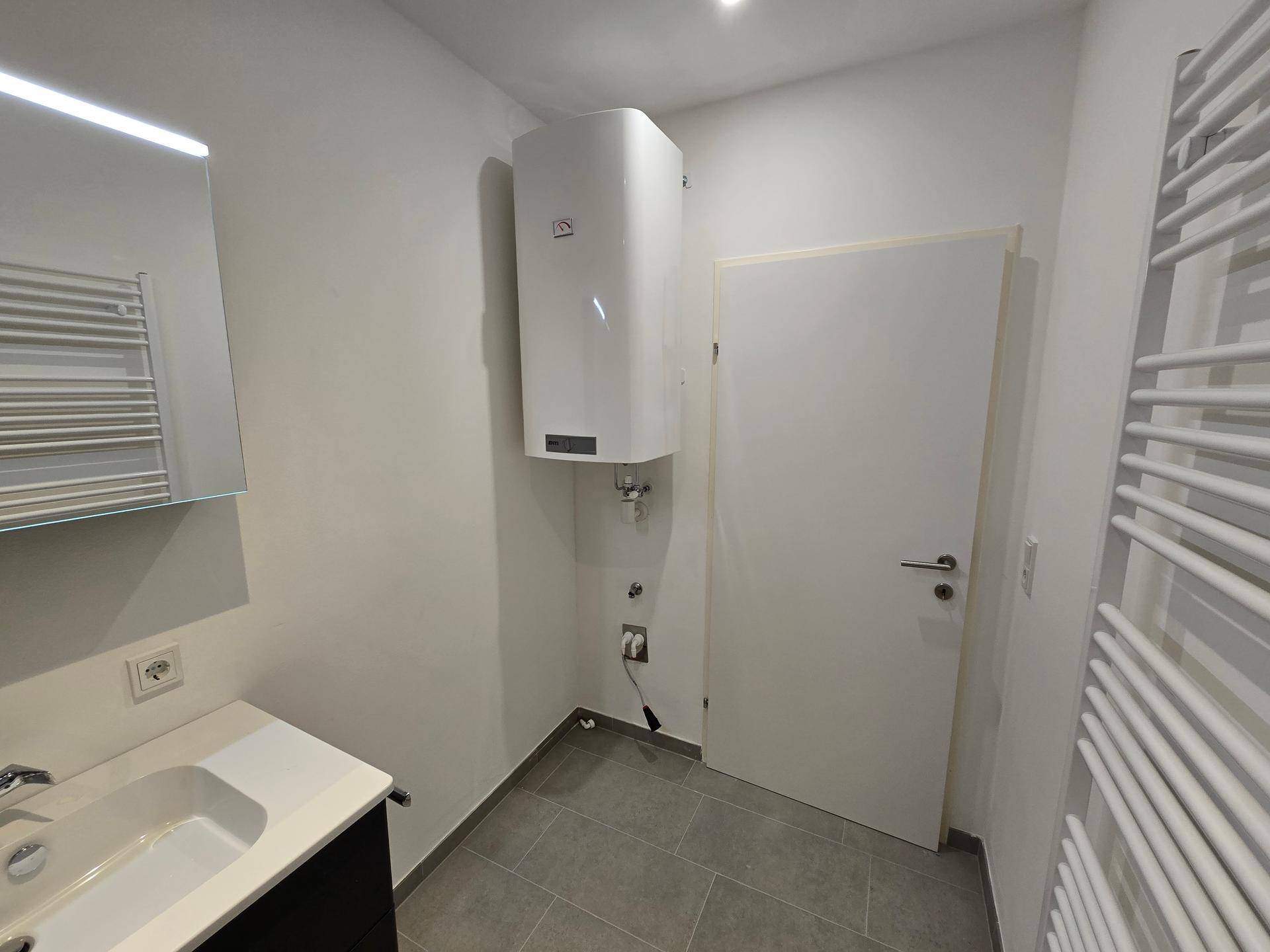 Modernes Badezimmer mit Waschbecken, Spiegelschrank und Warmwasserboiler an der Wand.