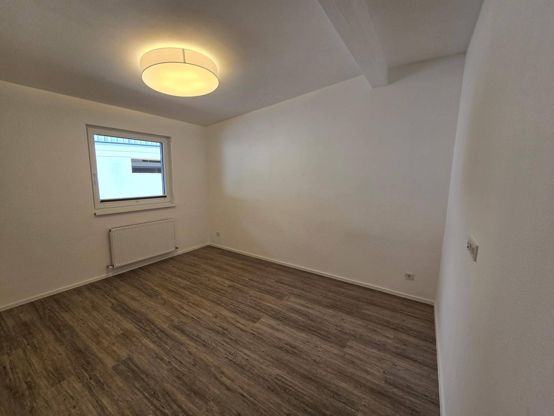 Ruhiges Schlafzimmer mit Laminatboden und einem Fenster, bietet vielseitige Nutzungsmöglichkeiten.