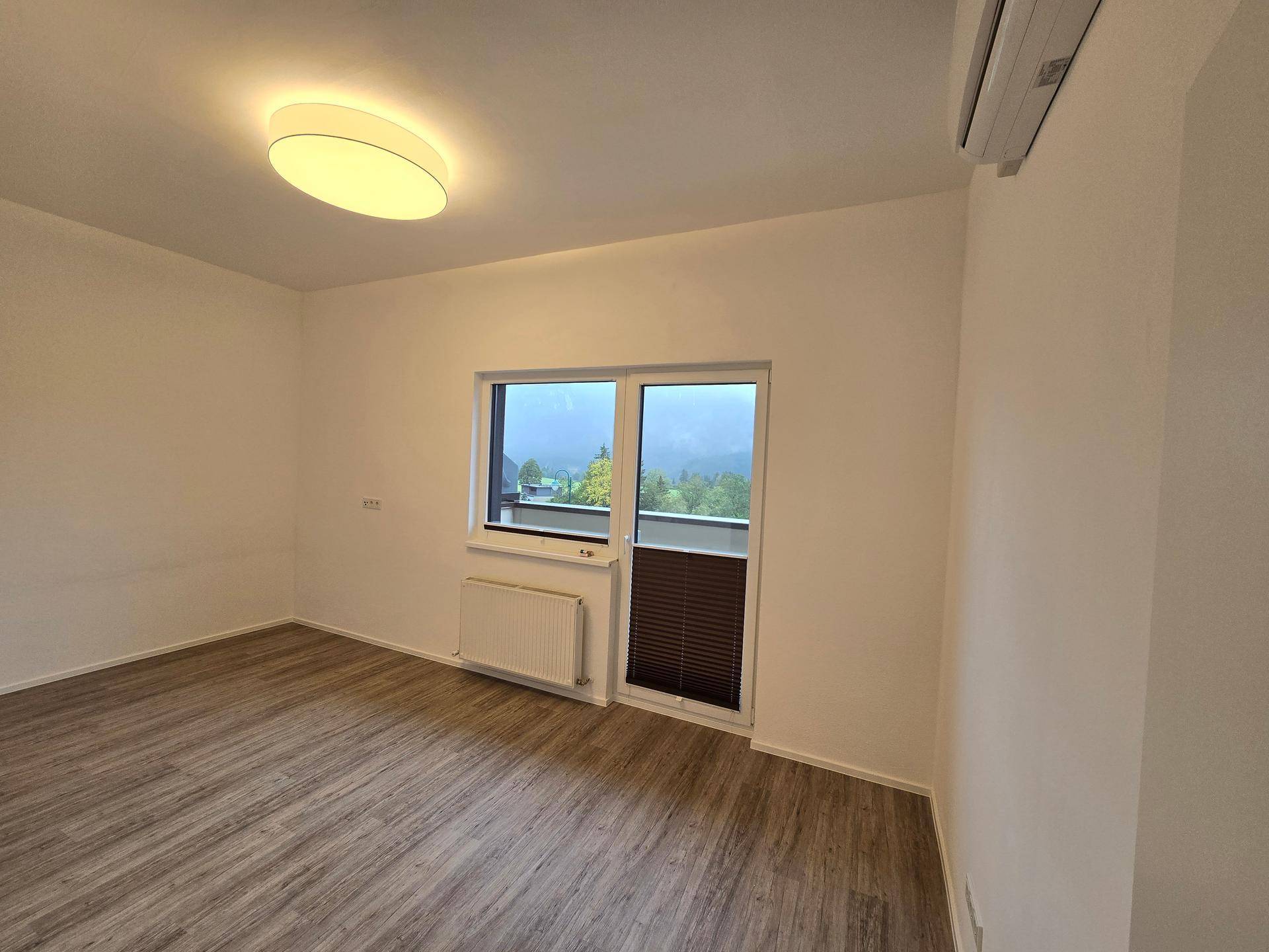 Helles Schlafzimmer mit Laminatboden, Klimaanlage und Fenster mit Bergblick.