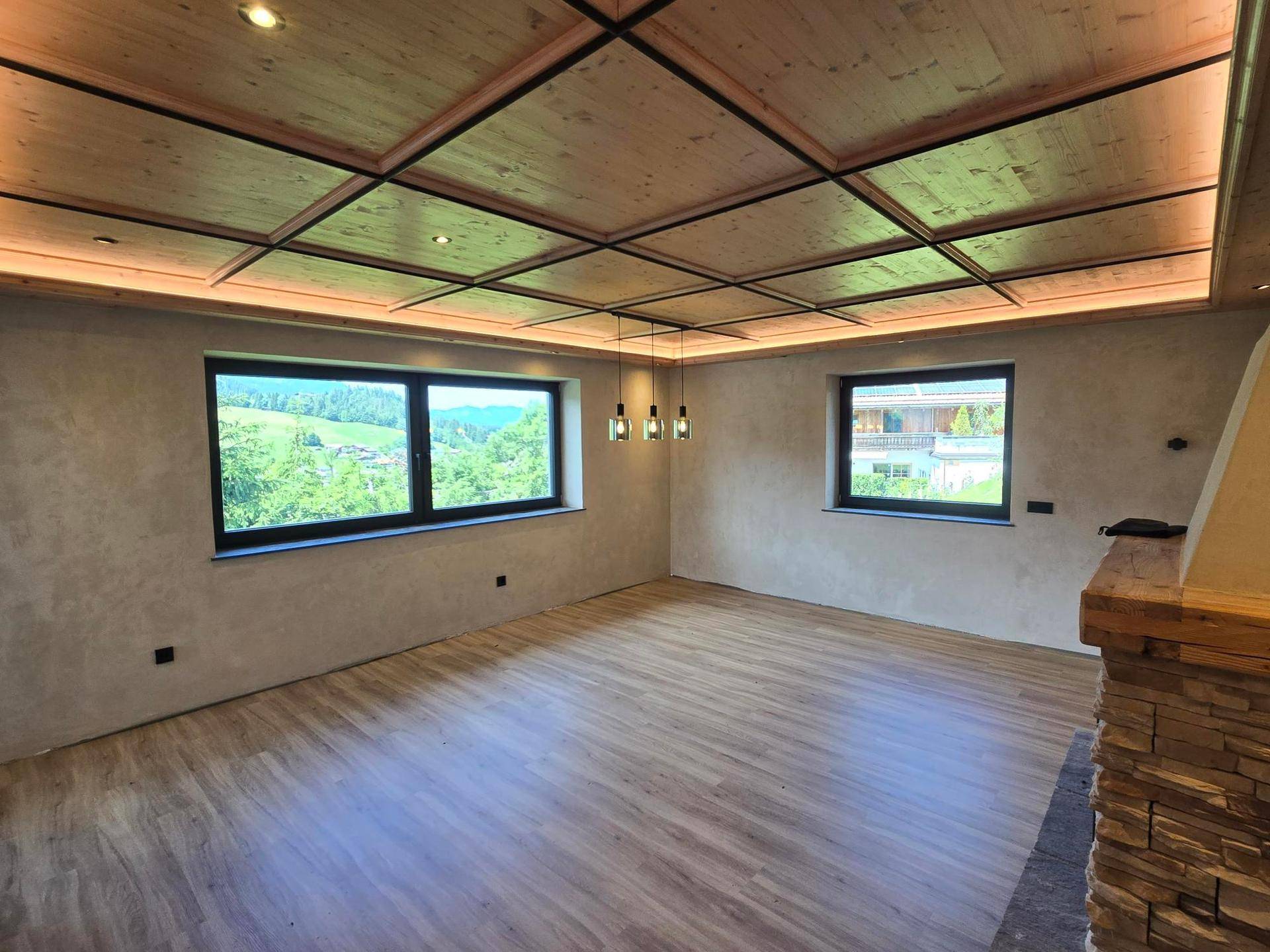 Geräumiges Wohnzimmer mit Holzboden, Kassettendecke und großen Fenstern mit Bergblick.
