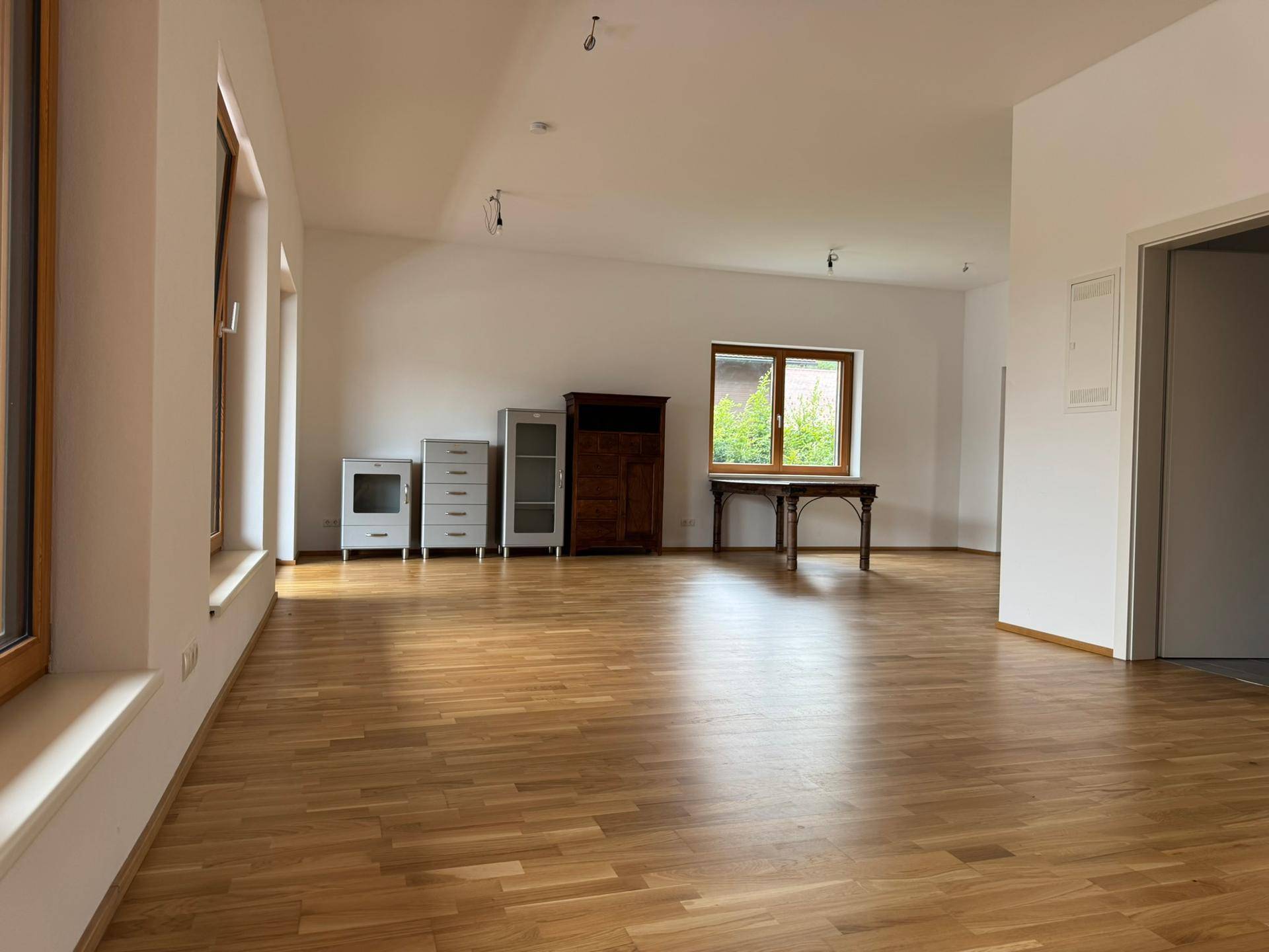 Geräumiger Wohnbereich mit hellem Holzboden und weißen Wänden, teilweise möbliert mit einem Holztisch.