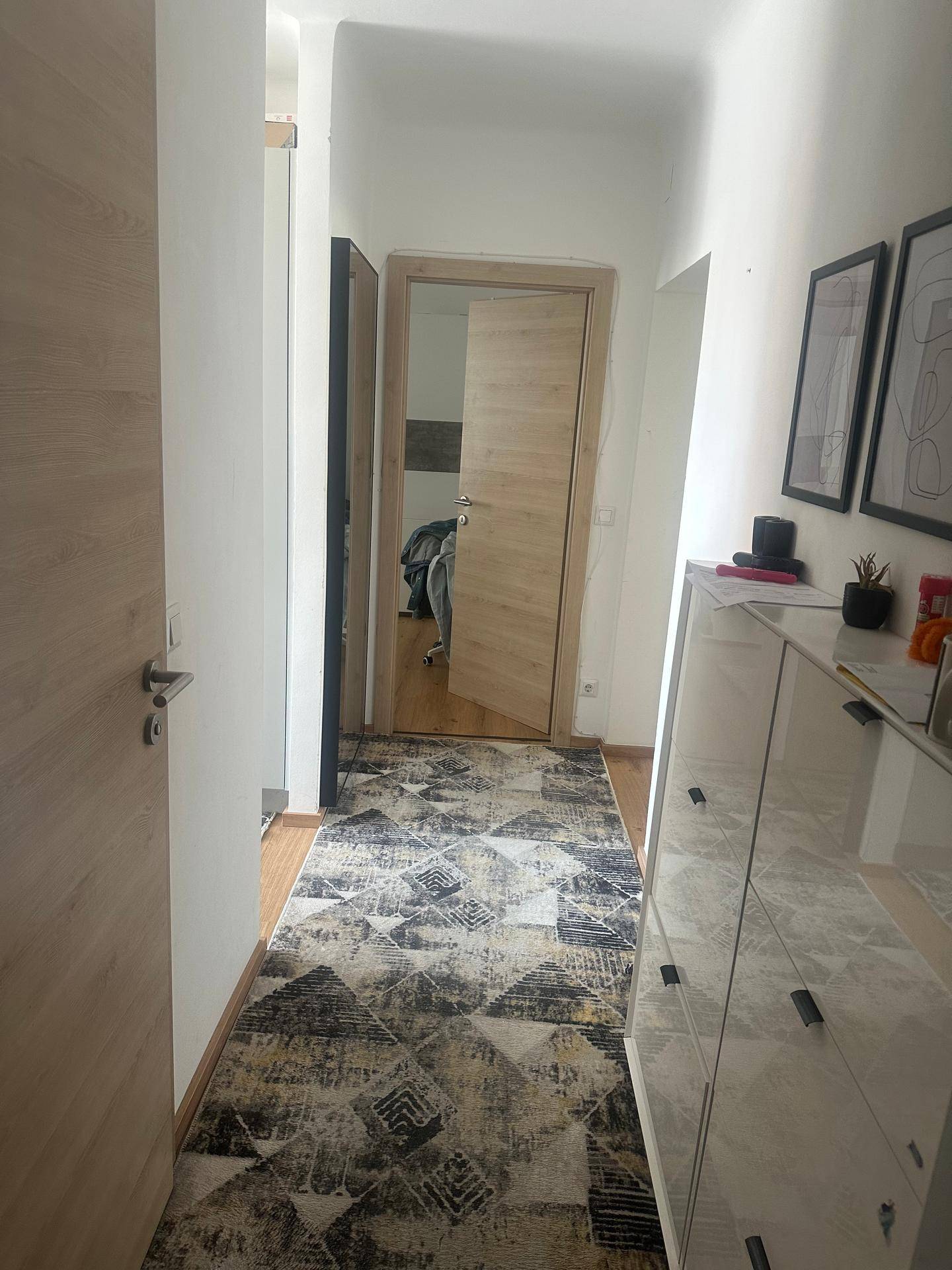 Heller Flur mit modernem Teppichläufer, weißer Kommode und Holzboden.