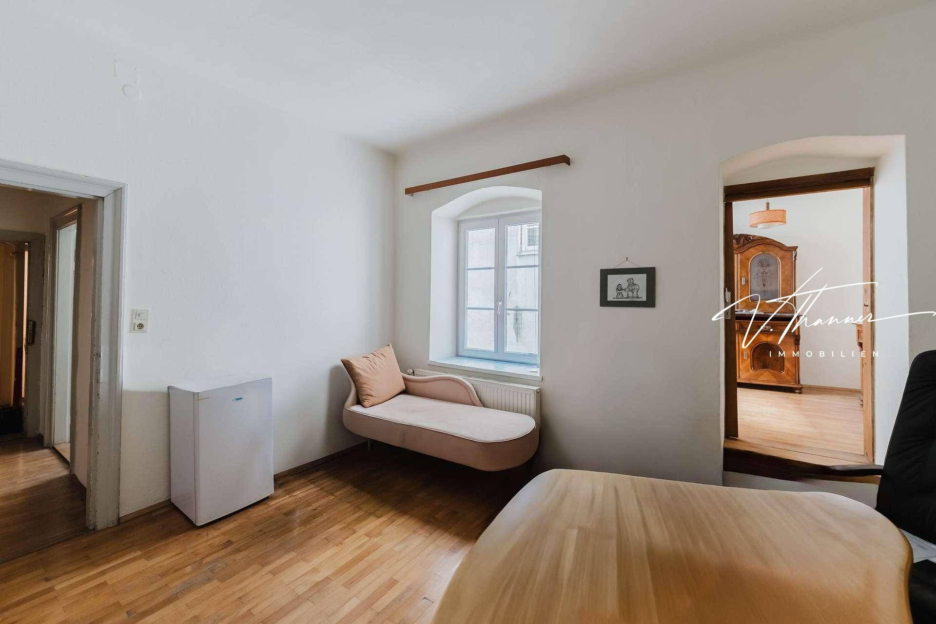 Helles Zimmer mit Holzboden, einer Chaiselongue und Zugang zu einem weiteren Raum.